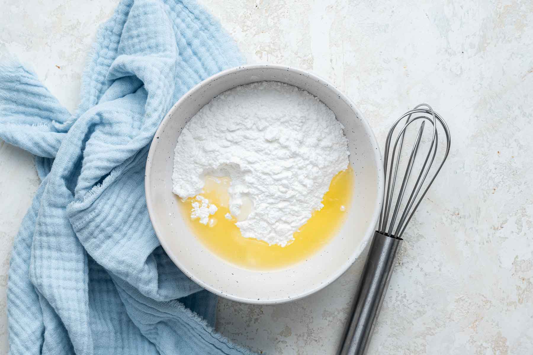 White bowl with powdered sugar and lemon juice with a whisk on the side.