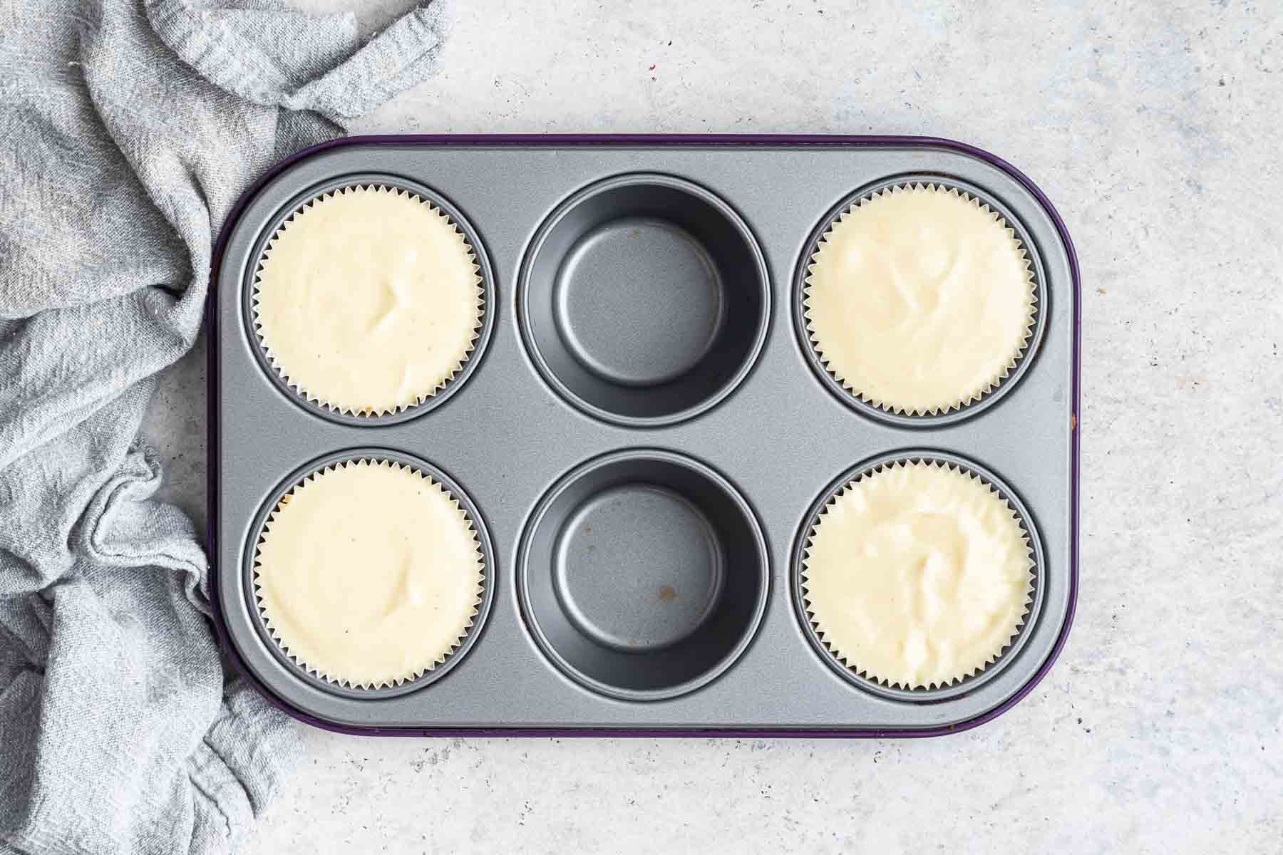Four raw mini cheesecakes in a muffin pan, before baking.