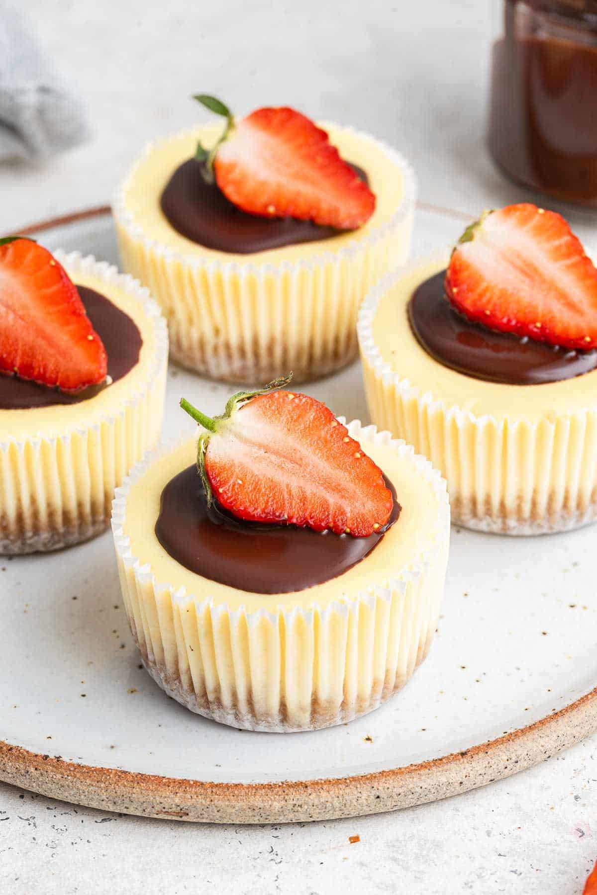 Vertical photo of four mini cheesecakes in muffin liners with a half strawberry on top.
