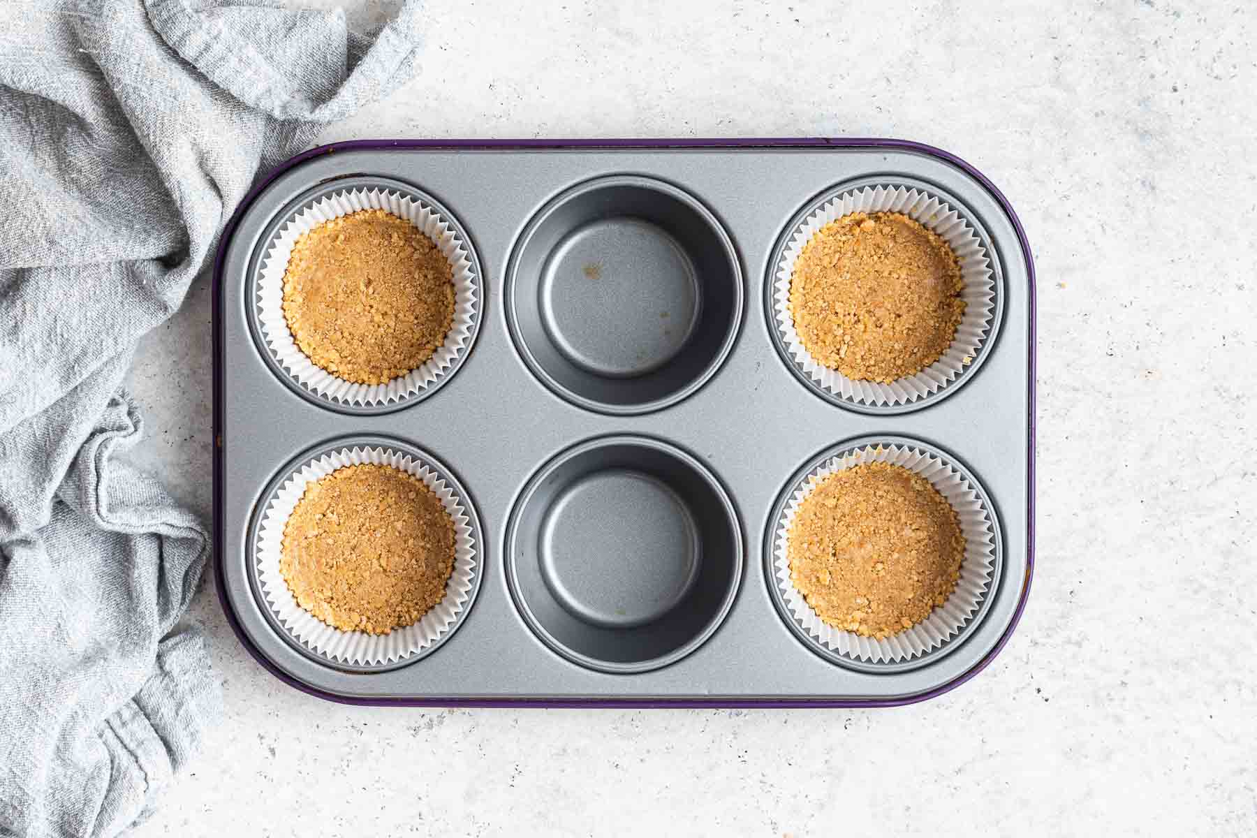 Four muffin cups with graham cracker crust packed inside.