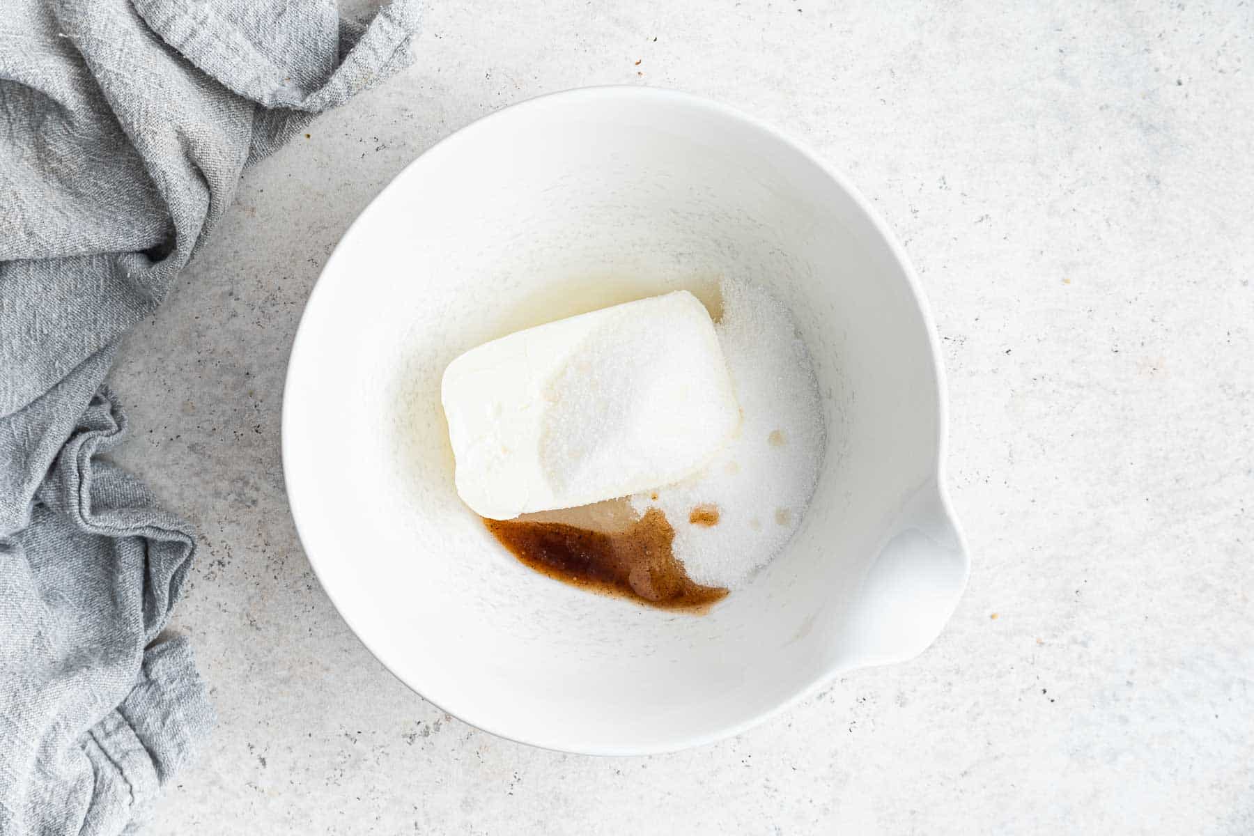 Cream cheese, sugar and vanilla in white bowl.