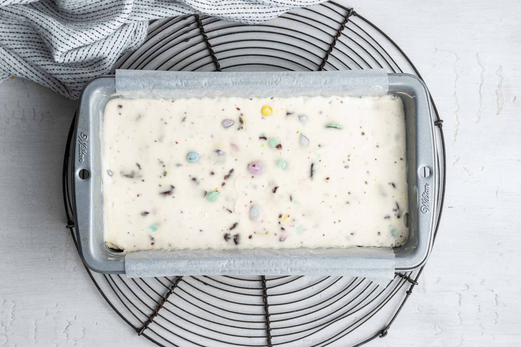 Mini egg cheesecake batter spread flat in a silver loaf pan.