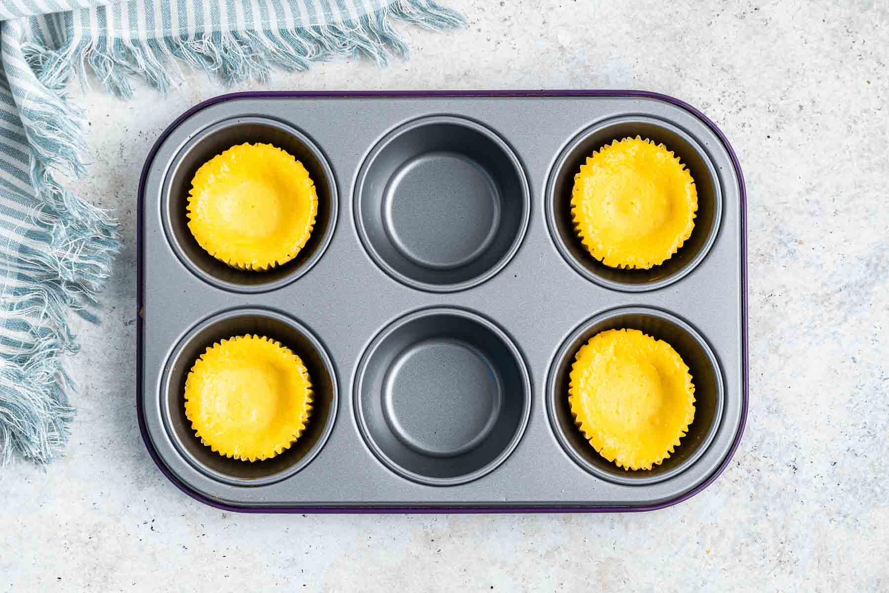 Freshly baked mini lemon cheesecakes in a muffin pan, cooling.