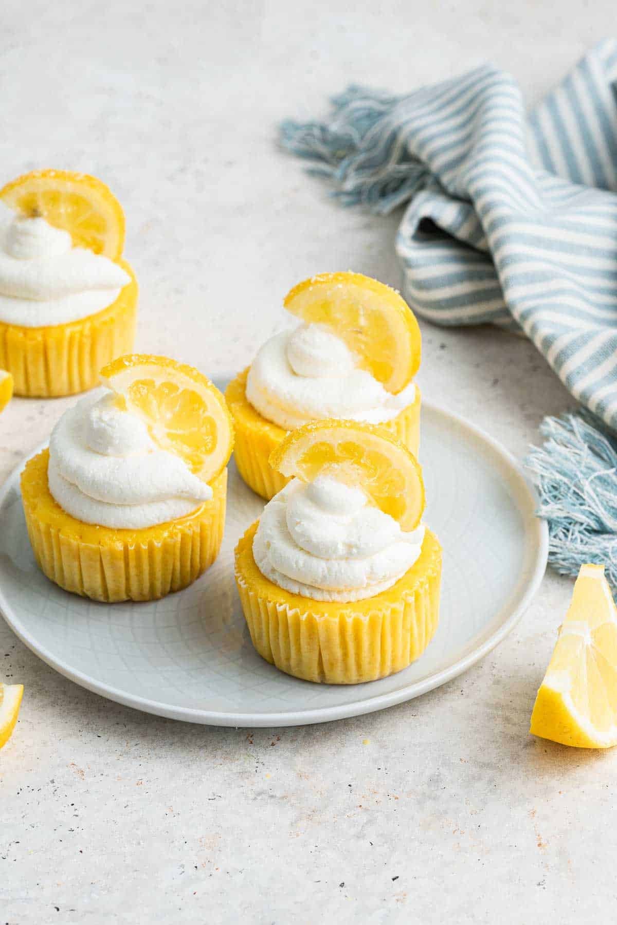 Three mini lemon cheesecakes on a grey plate garnished with whipped cream and lemon slices.