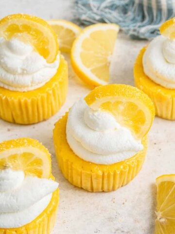 Four yellow lemon cheesecakes with whipped cream and a lemon slice on top.