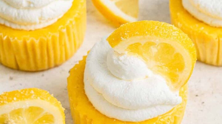 Four yellow lemon cheesecakes with whipped cream and a lemon slice on top.