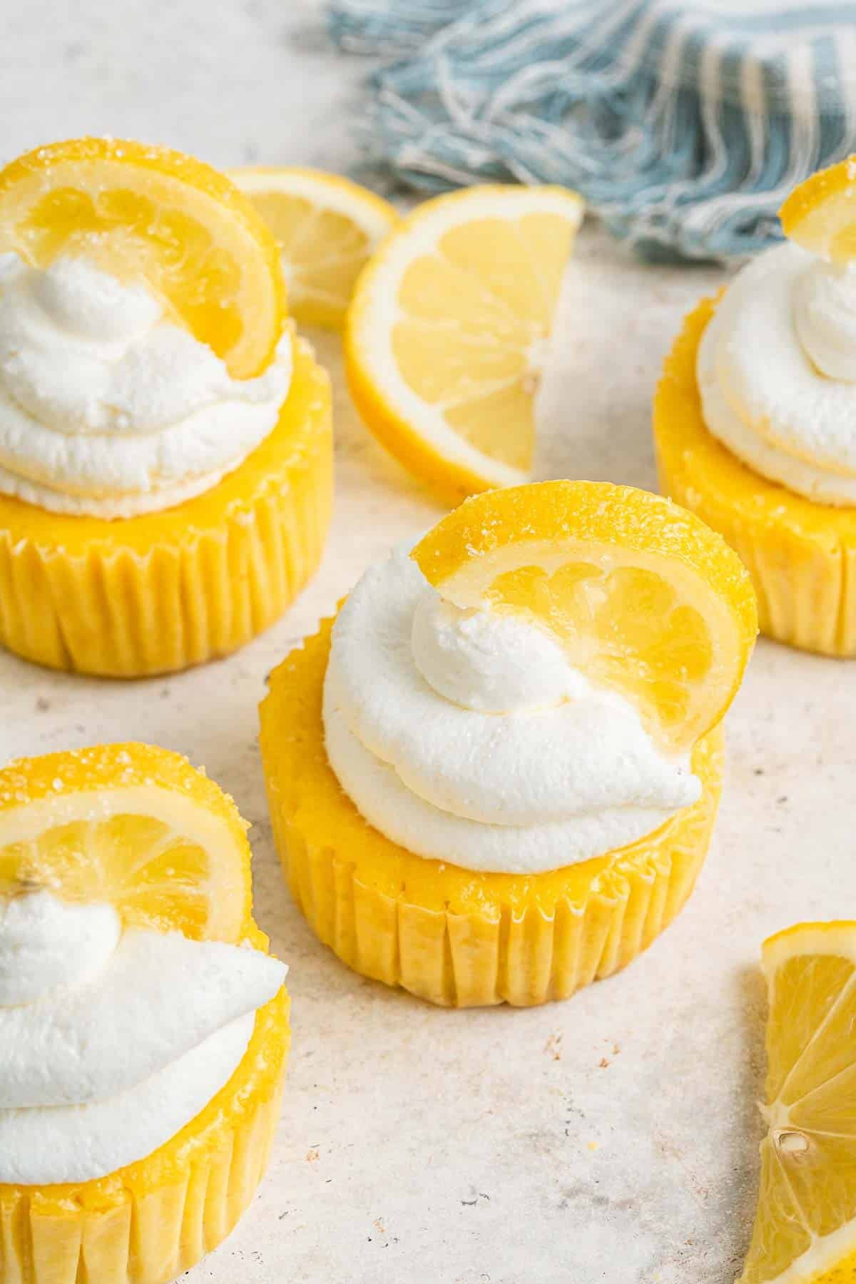 Four yellow mini lemon cheesecakes with whipped cream and a lemon slice on top.