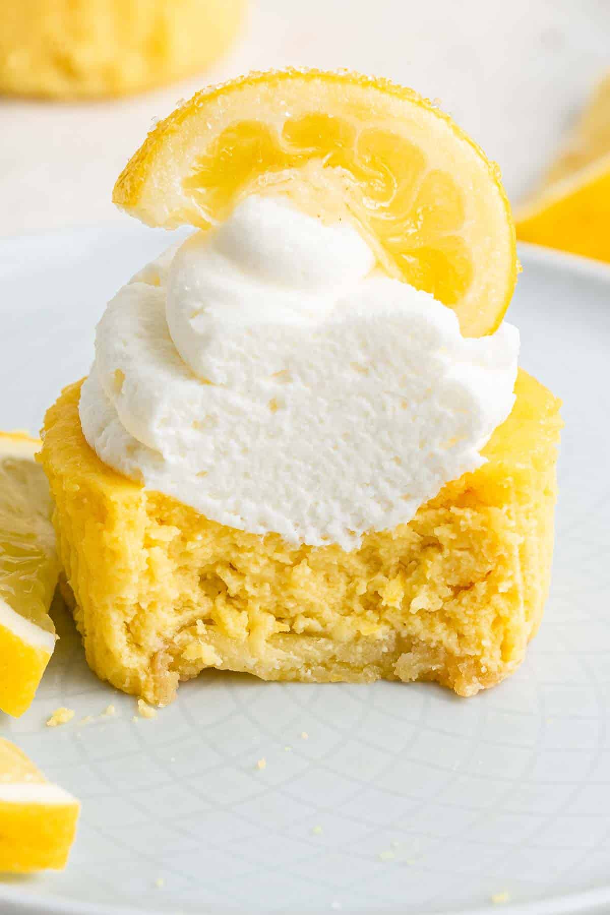 Close up of yellow cupcake cheesecake with whipped cream and lemon slice on top, cut in half.