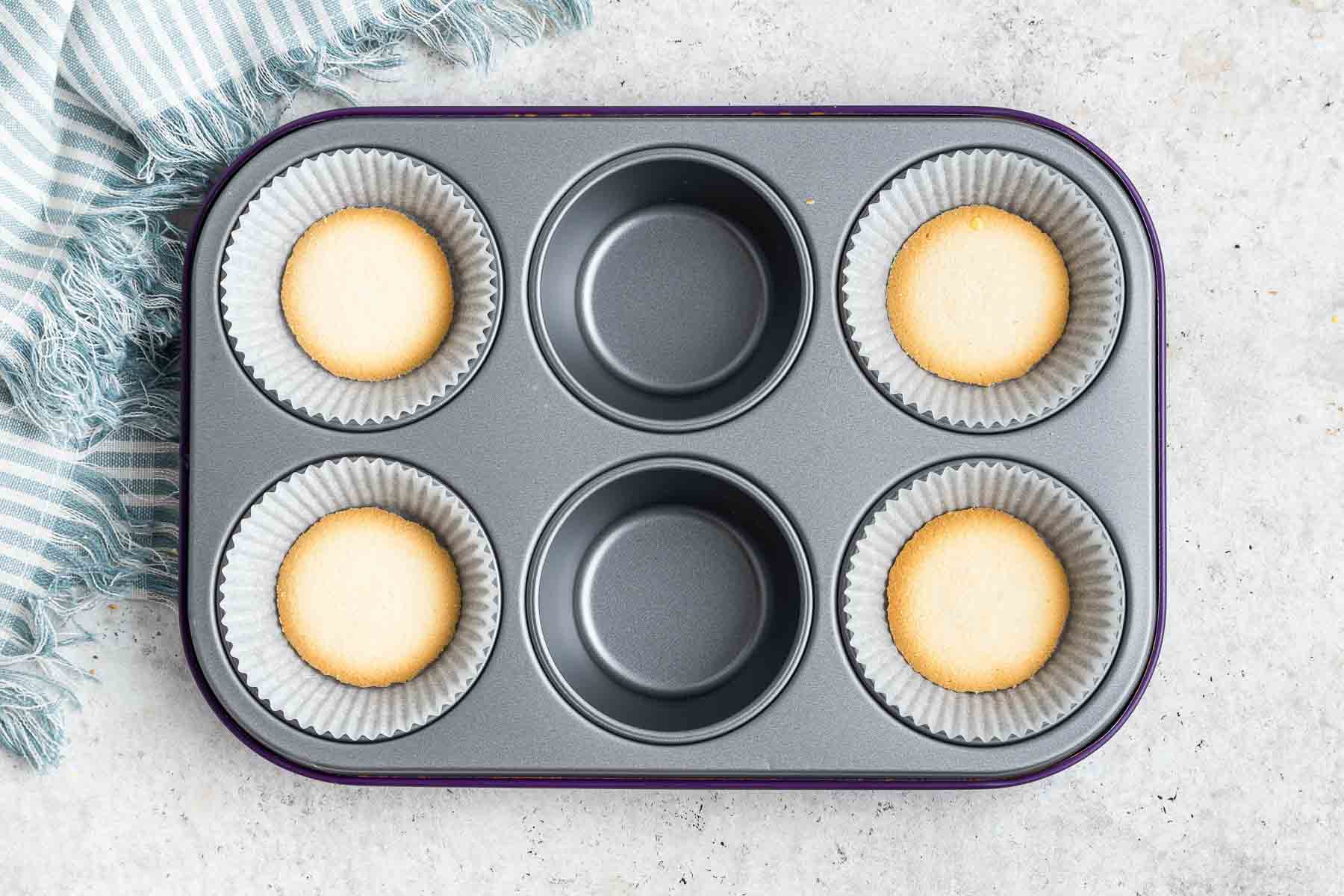 Four pale cookies in the bottom of muffin cups.