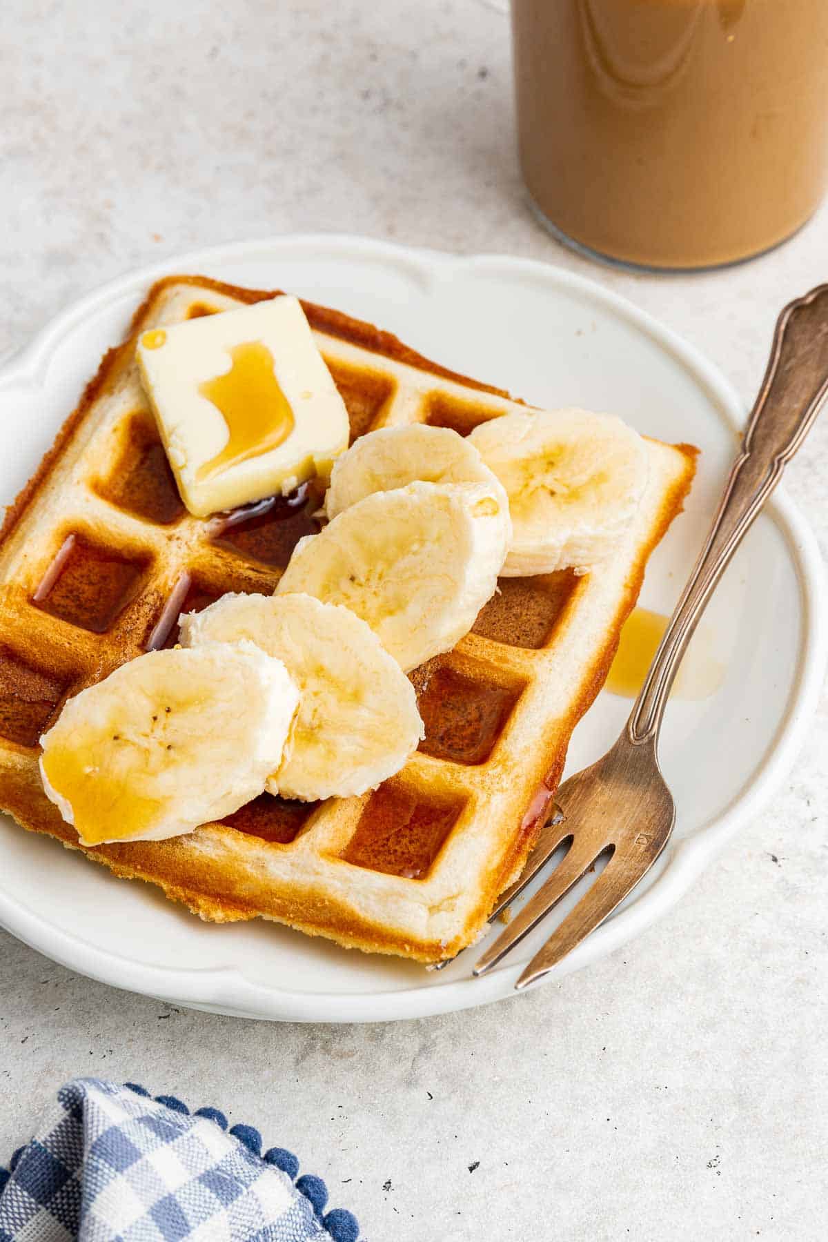 A single waffle for one person on white plate with coffee and fork on side.
