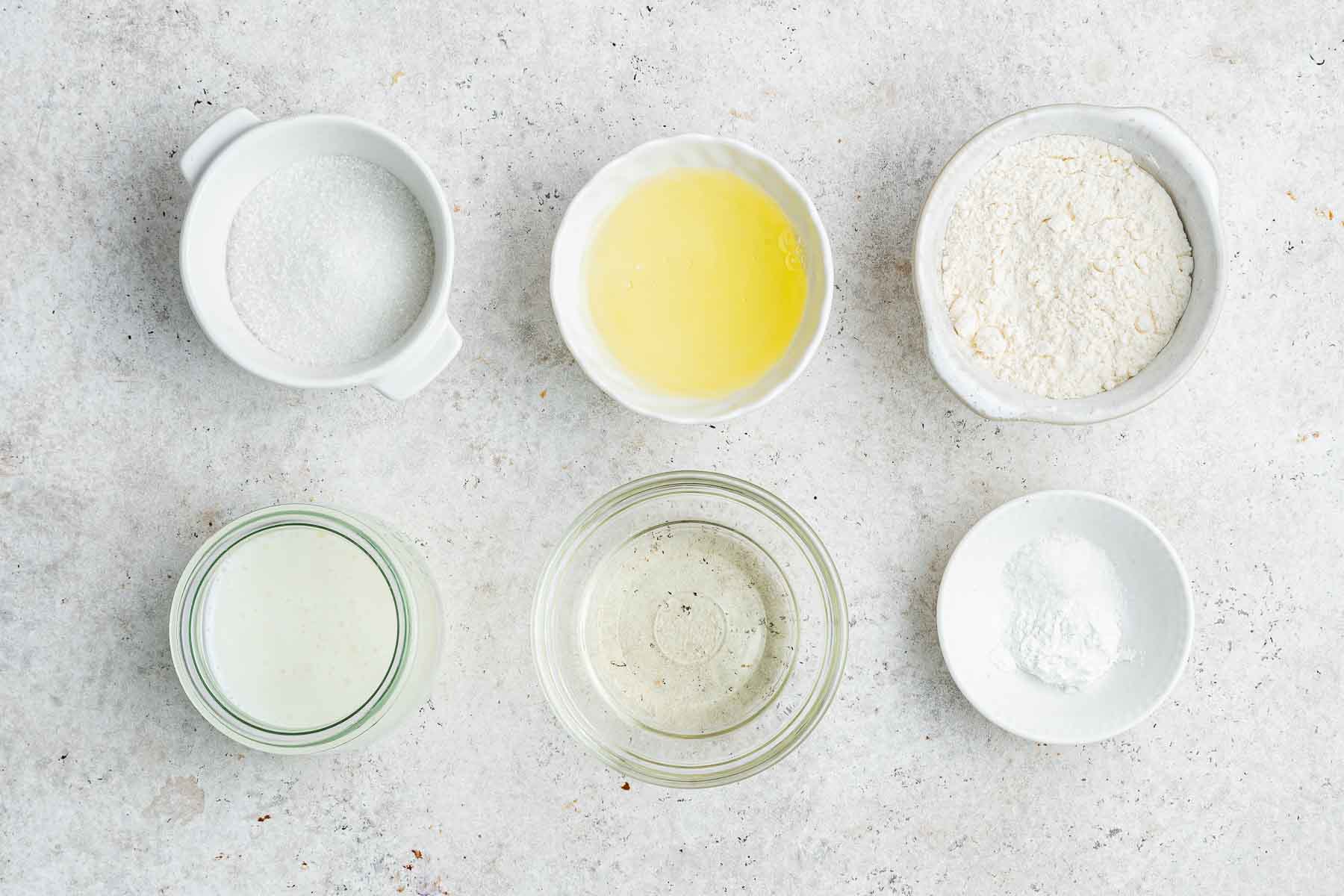 Small bowls with flour, egg white, buttermilk, and sugar on grey marble counter.