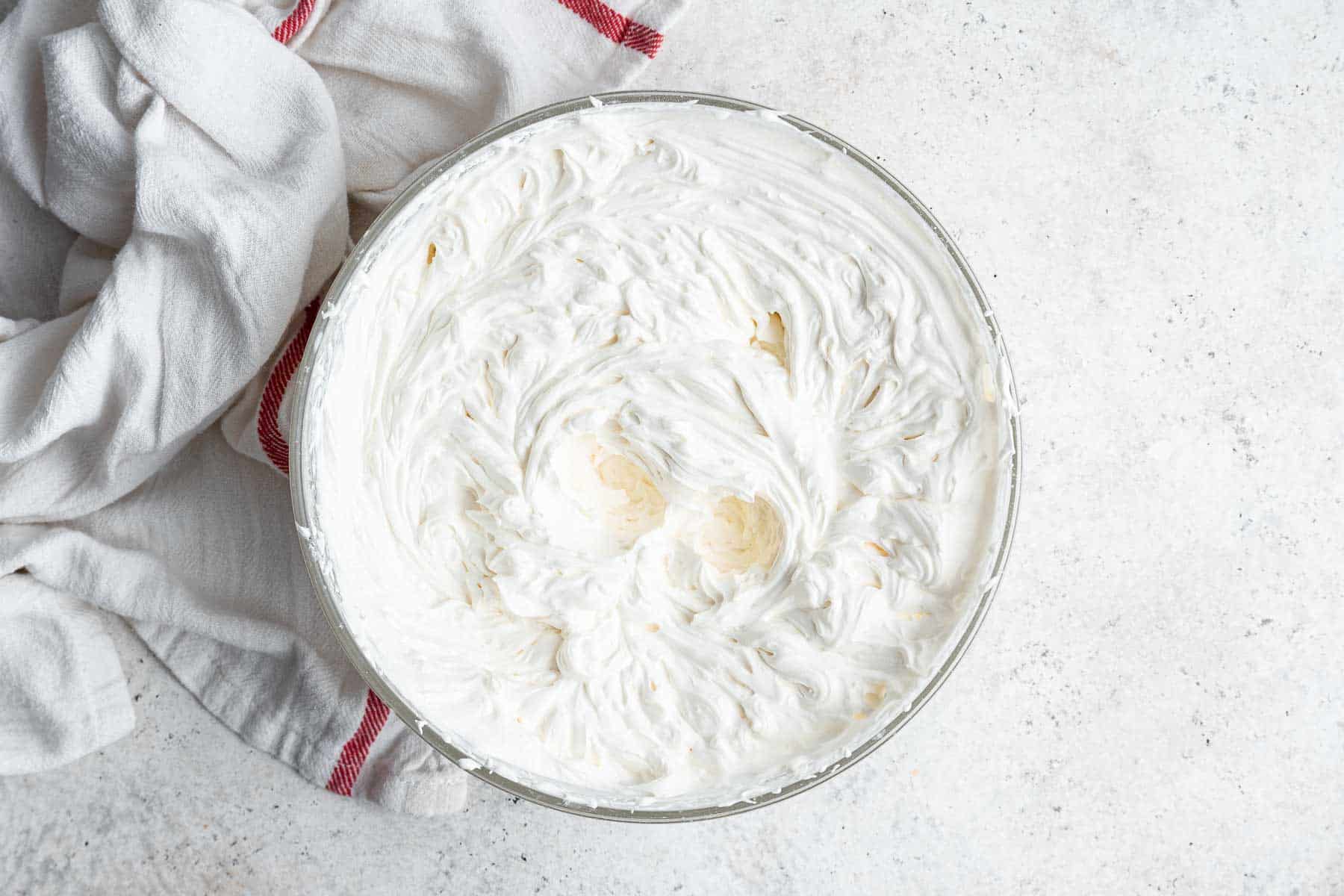 Fluffy white filling for a crepe cake in a clear bowl.