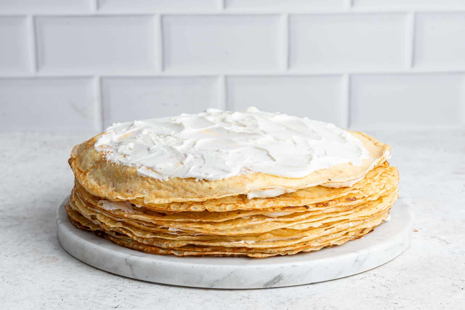 Stacked crepes with cream, making a layer cake on a plate.