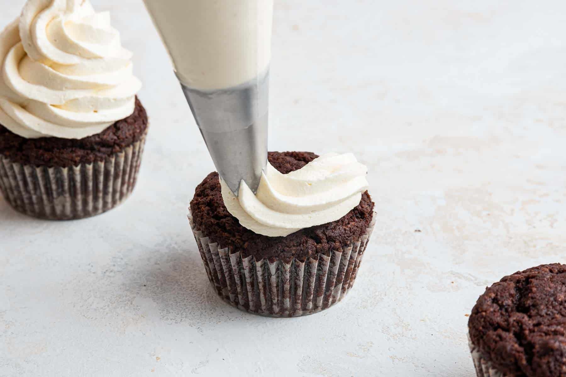 Piping bag putting icing on chocolate cupcake from above.