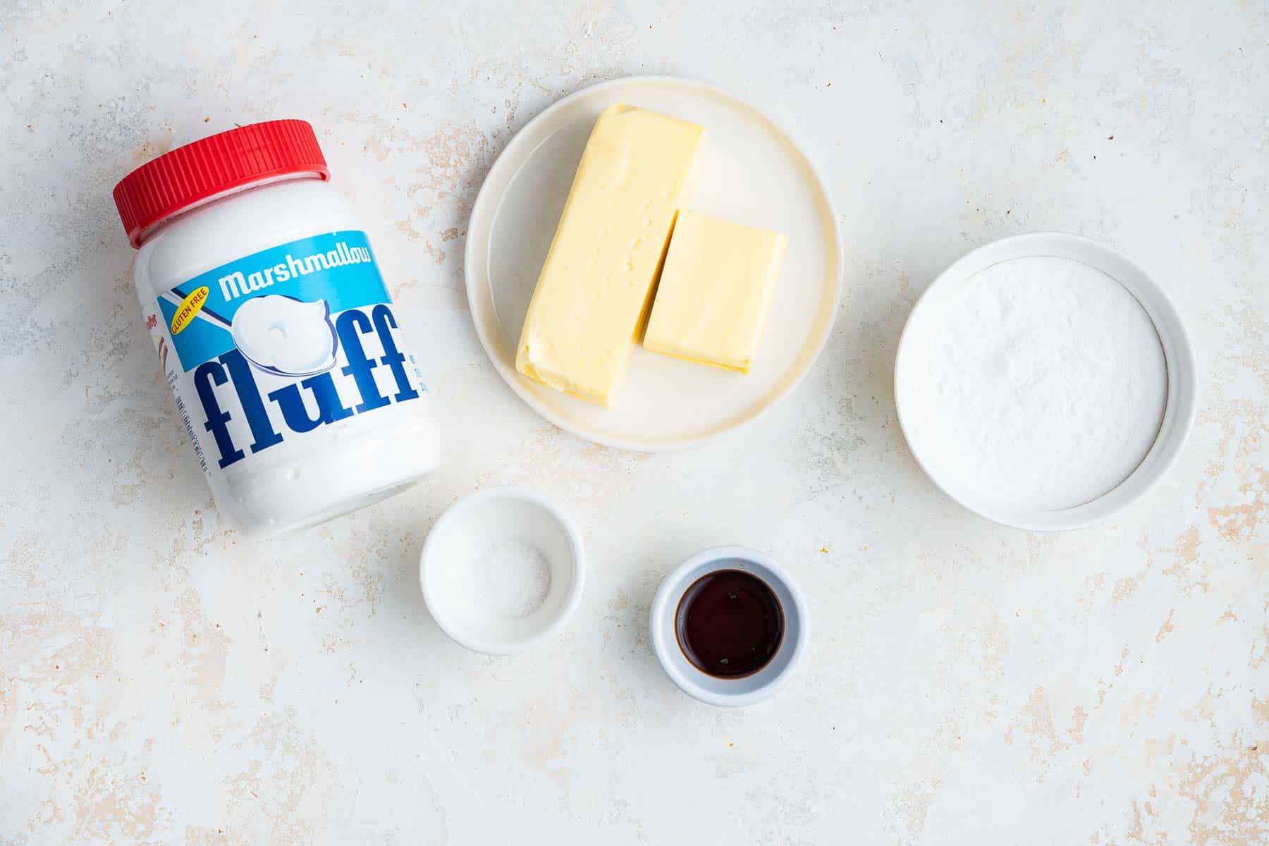 Photo of marshmallow fluff, butter, powdered sugar, salt and vanilla on grey counter.