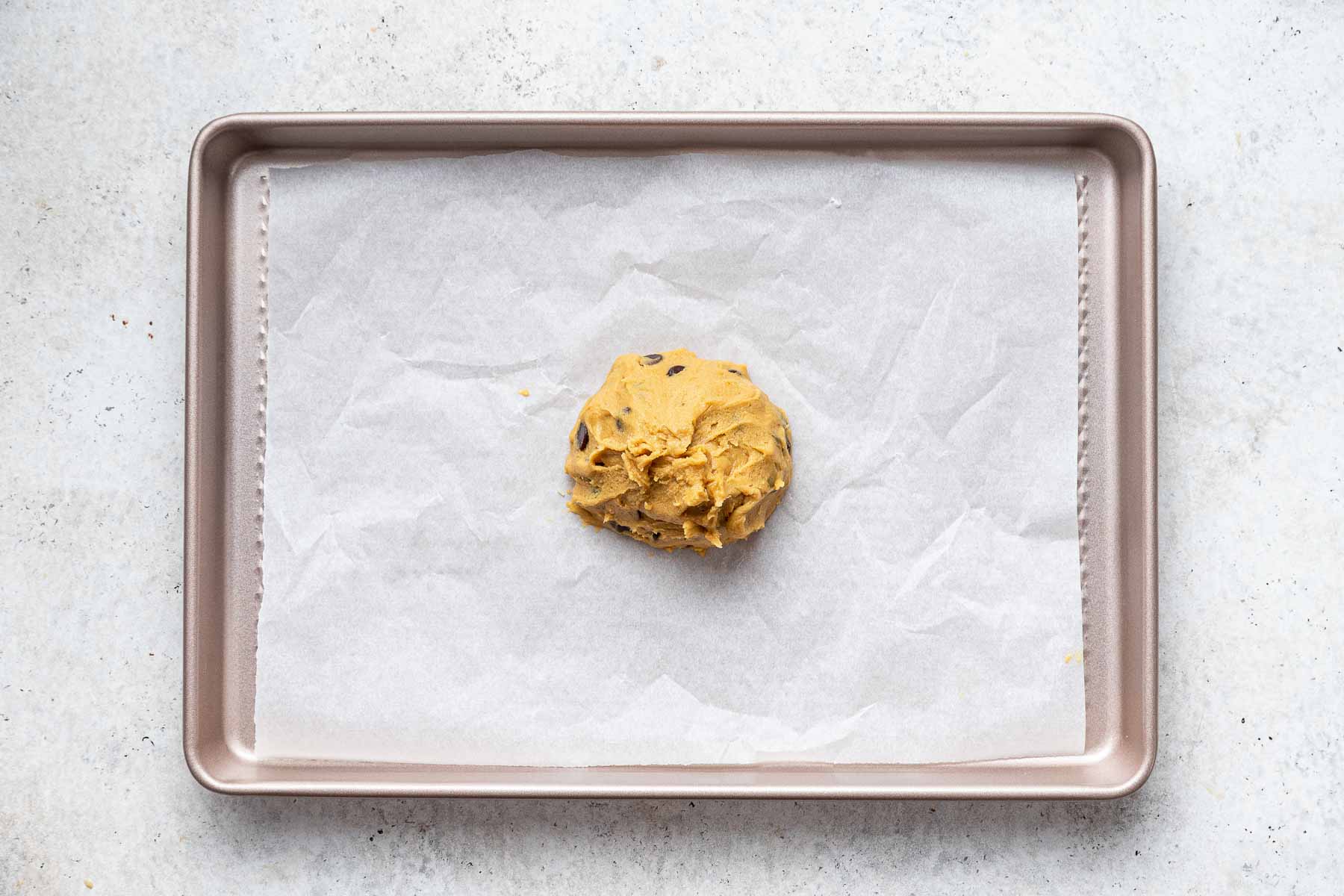 One single mound of raw cookie dough on small baking sheet lined with parchment paper.