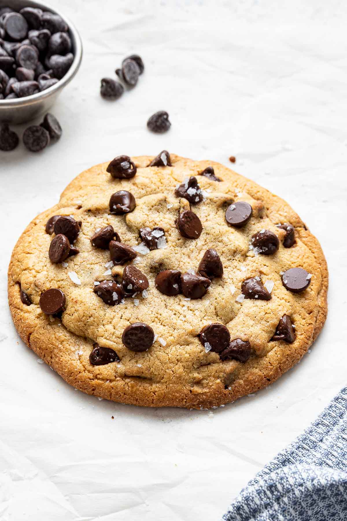 A single serve chocolate chip cookie on sheet with chocolate chips on the side.
