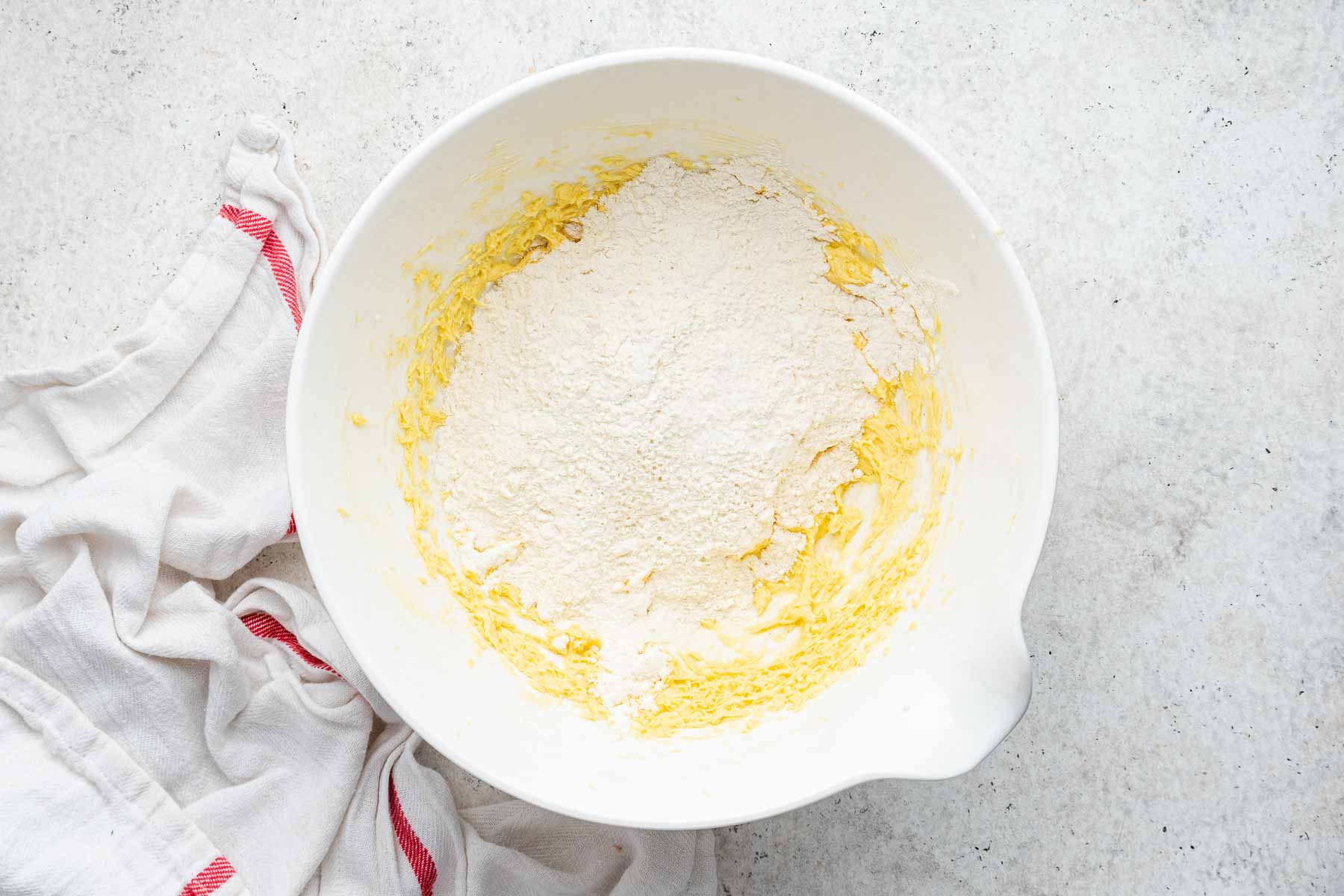 White flour on top of yellow cookie dough in white bowl.