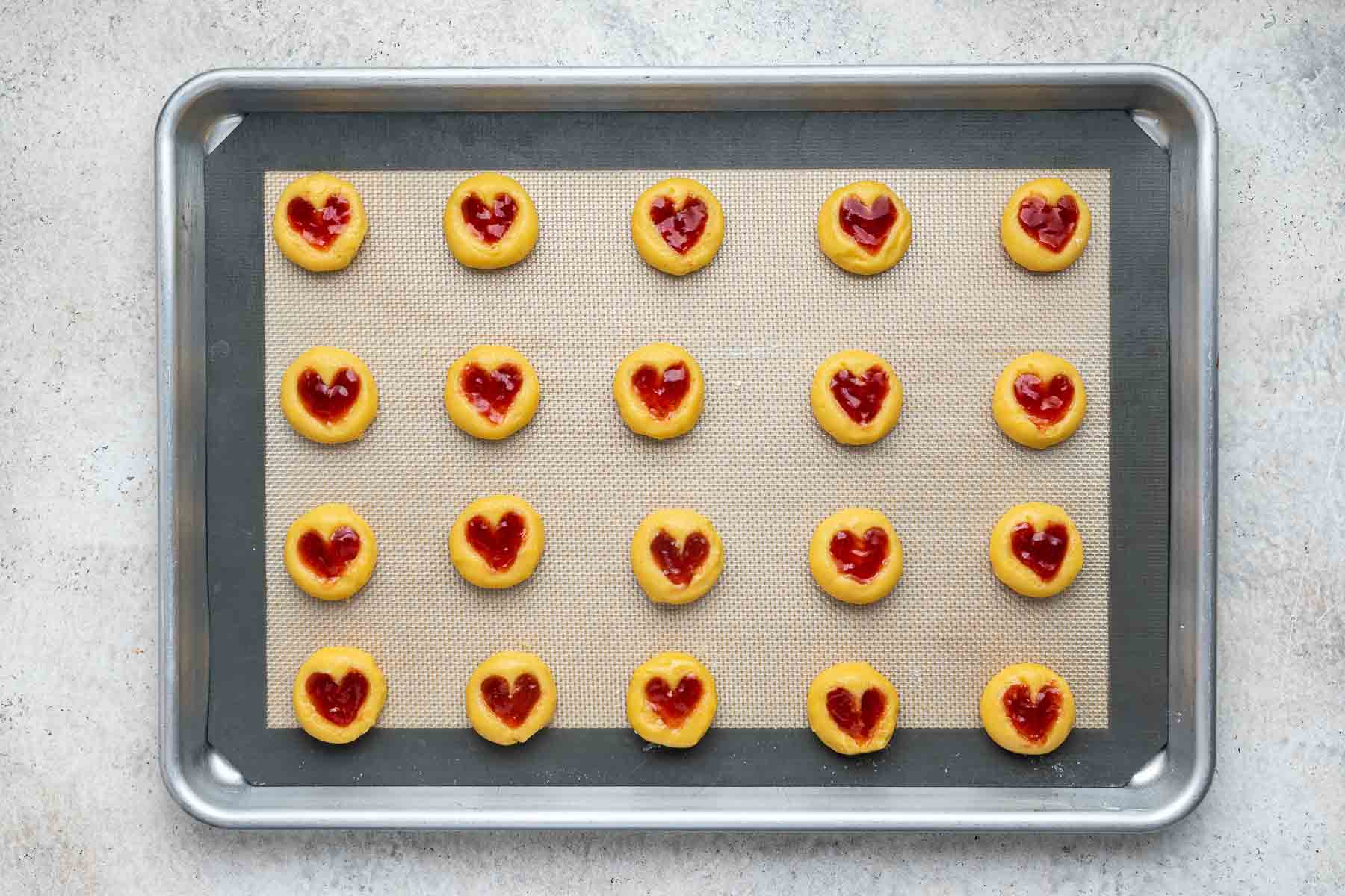 Round yellow cookies with heart jam centers on baking sheet.