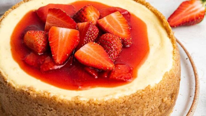 Small 6 inch cheesecake recipe with strawberry sauce on top and a tall crust.