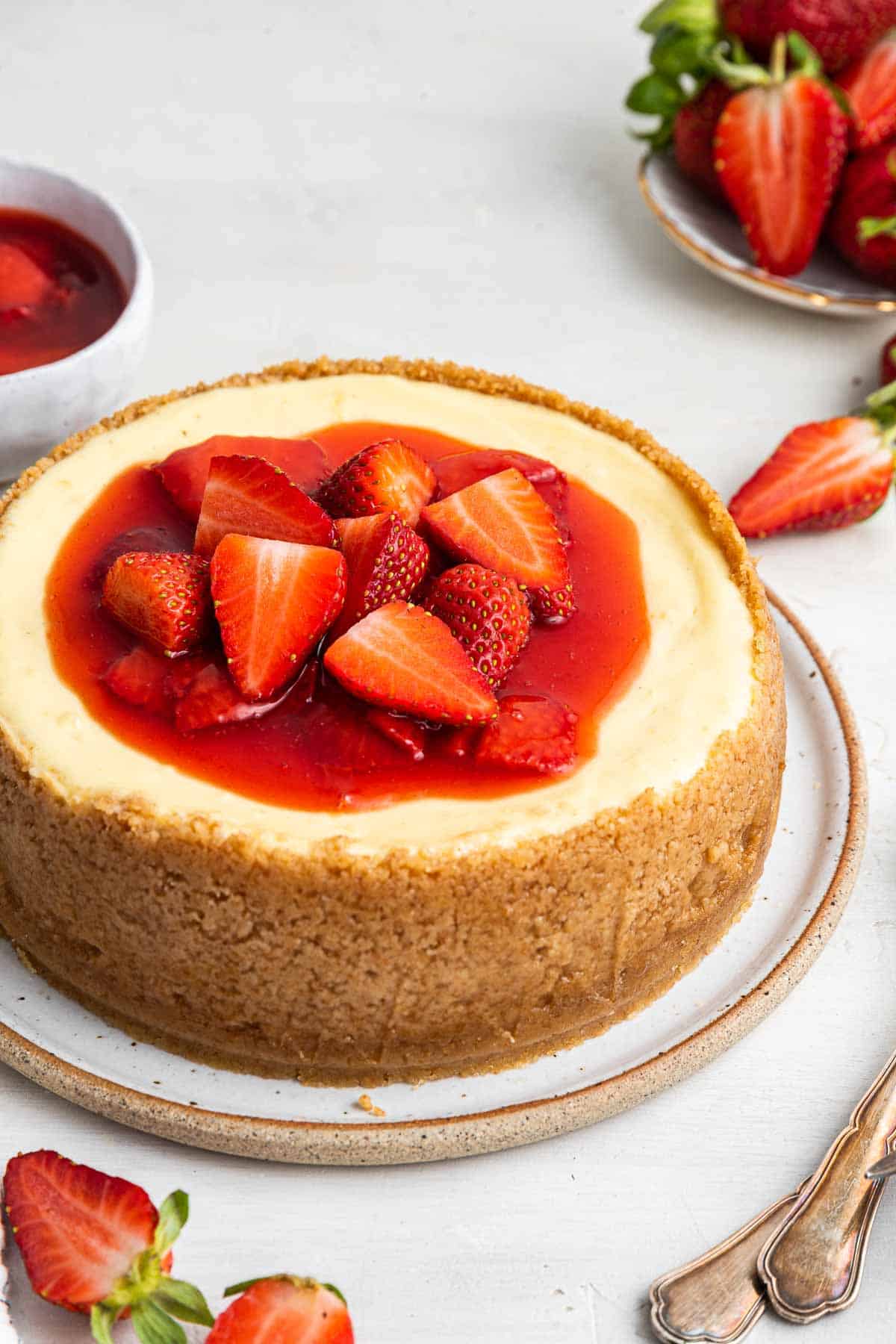 Small 6 inch cheesecake recipe with strawberry sauce on top and a tall crust.