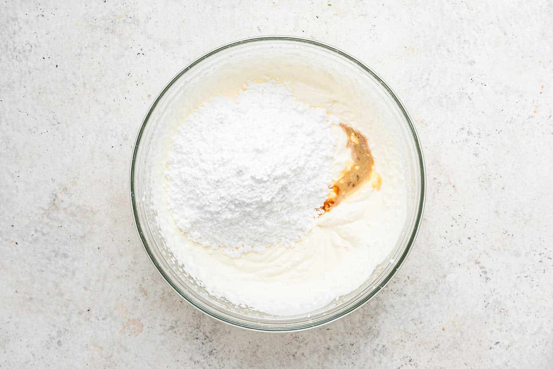 Whipping cream with powdered sugar and vanilla in glass bowl.