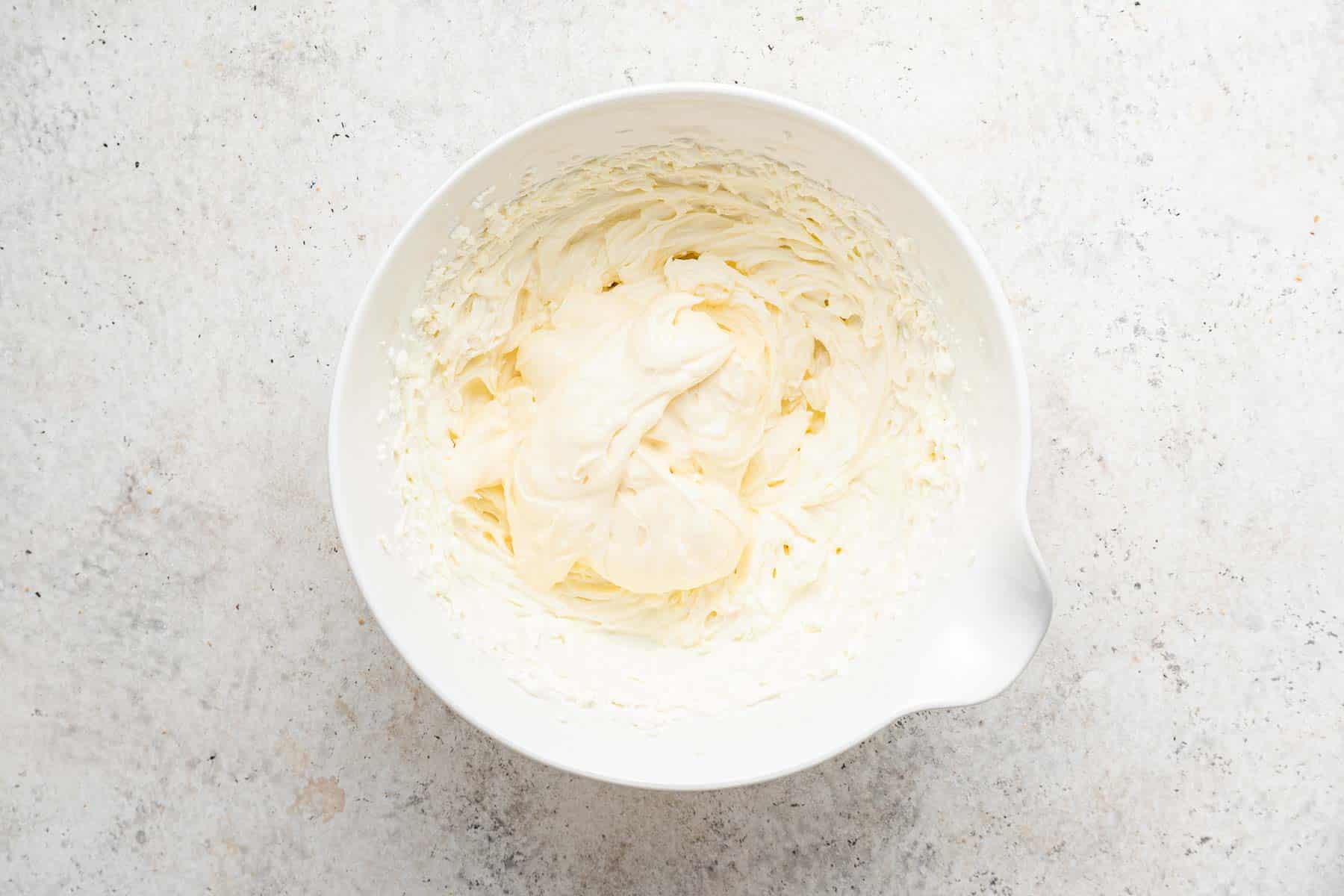 Softened cream cheese beaten in white bowl.