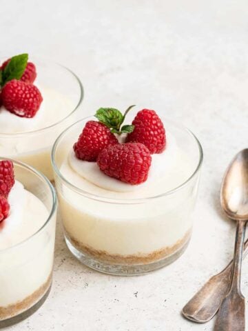 Three cheesecake cups consisting of clear glasses with white cake inside and raspberries on top.
