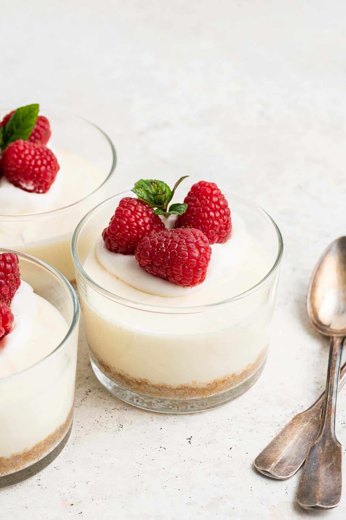 Three cheesecake cups consisting of clear glasses with white cake inside and raspberries on top.