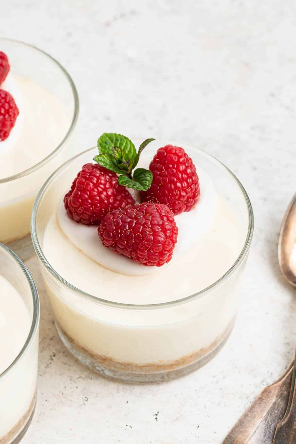 Closeup of cheesecake cups garnished with fresh raspberries and mint leaves.