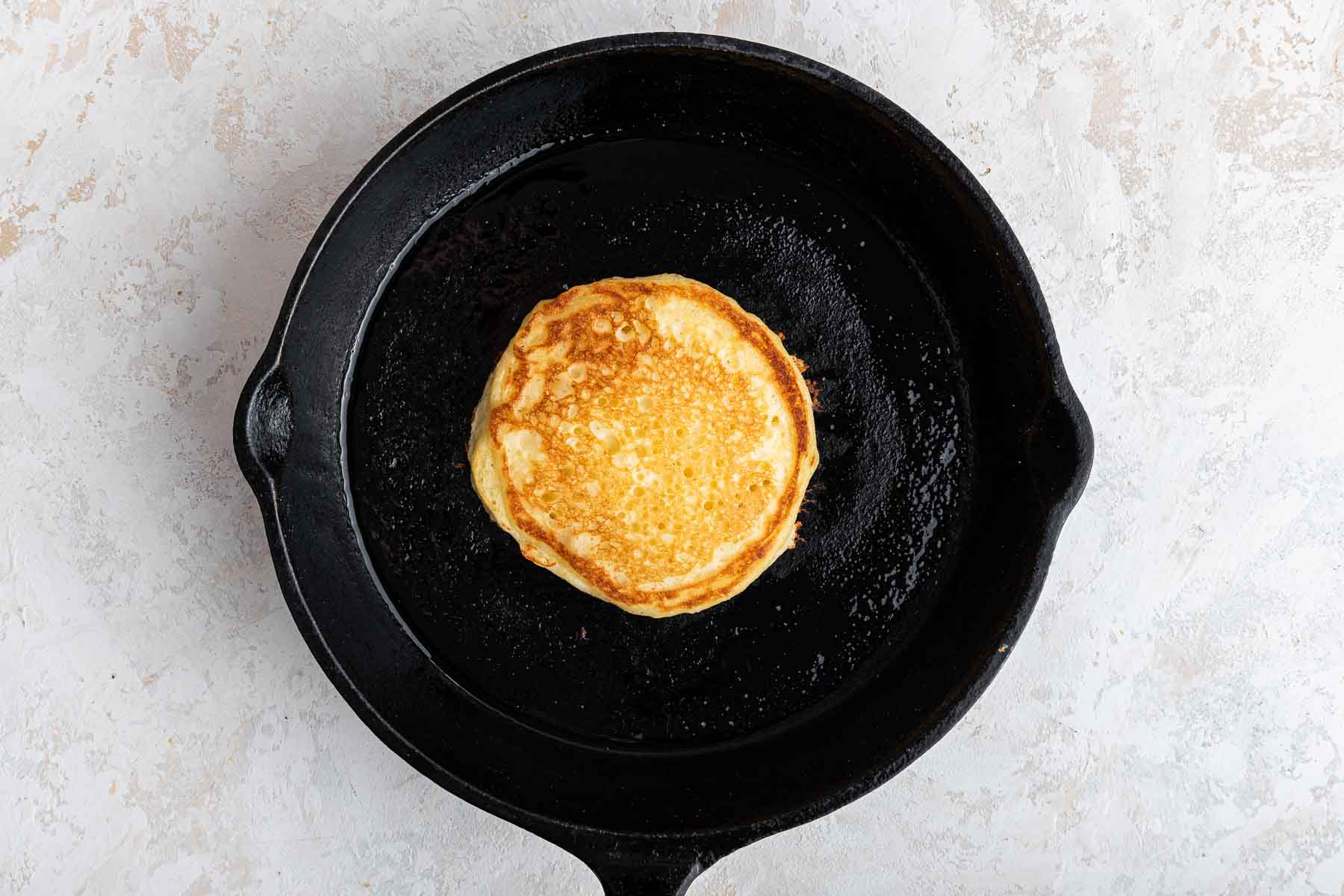 One flipped pancake in black cast iron skillet.
