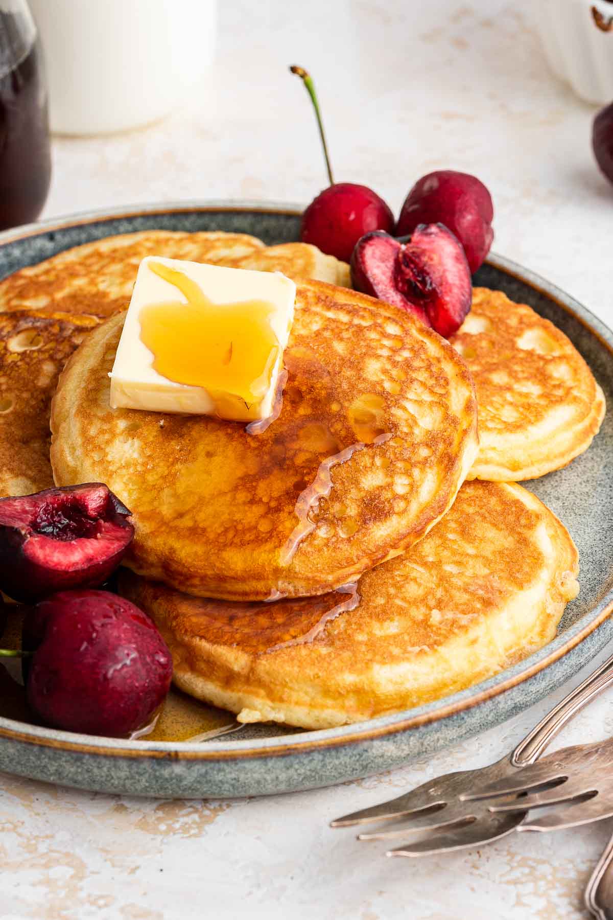 Plate of round pancakes with fresh cherries and butter on top.