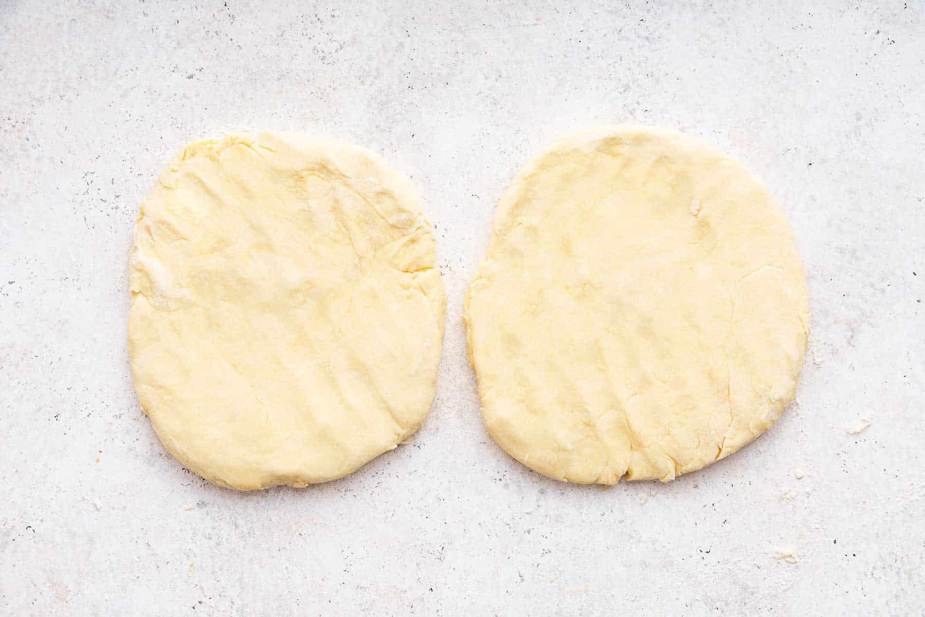 Two round pastry crusts, next to each other on a marble board.