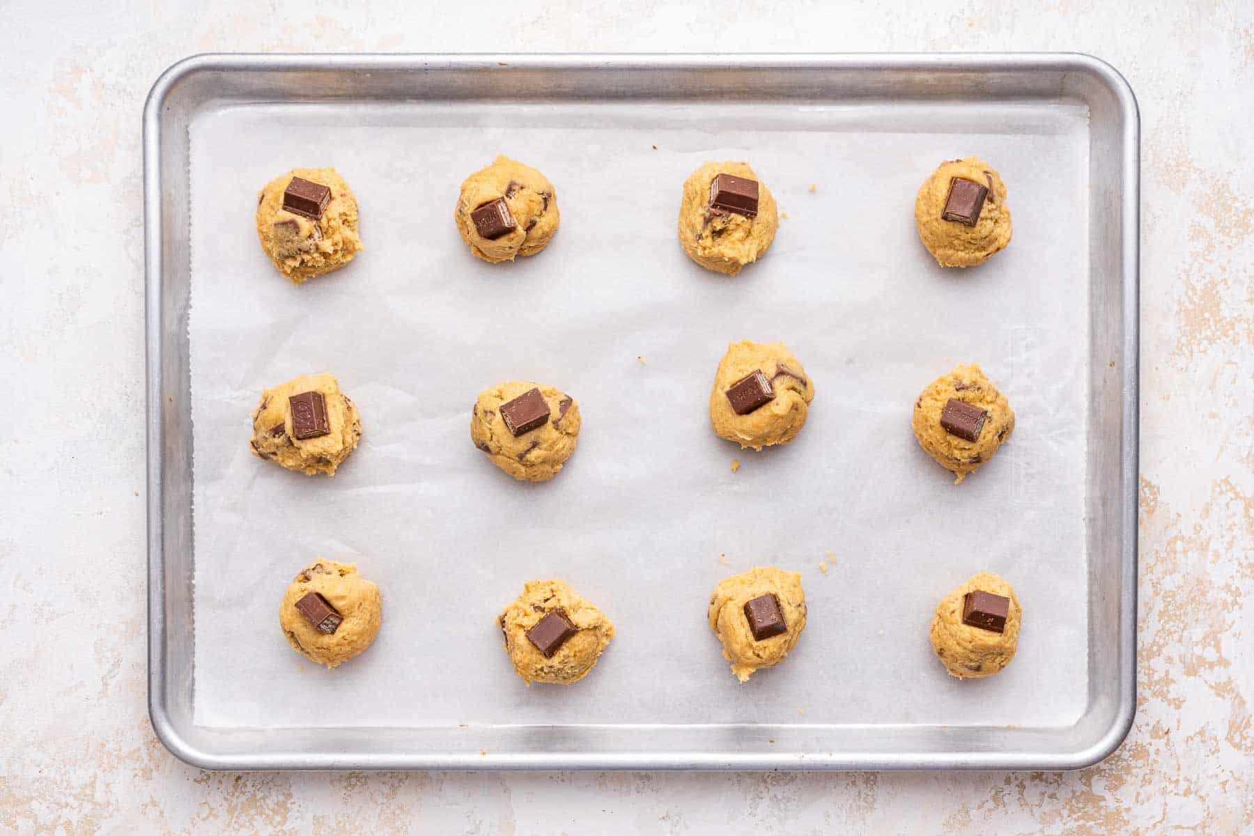 Twelve cookies on a baking sheet, before being baked.