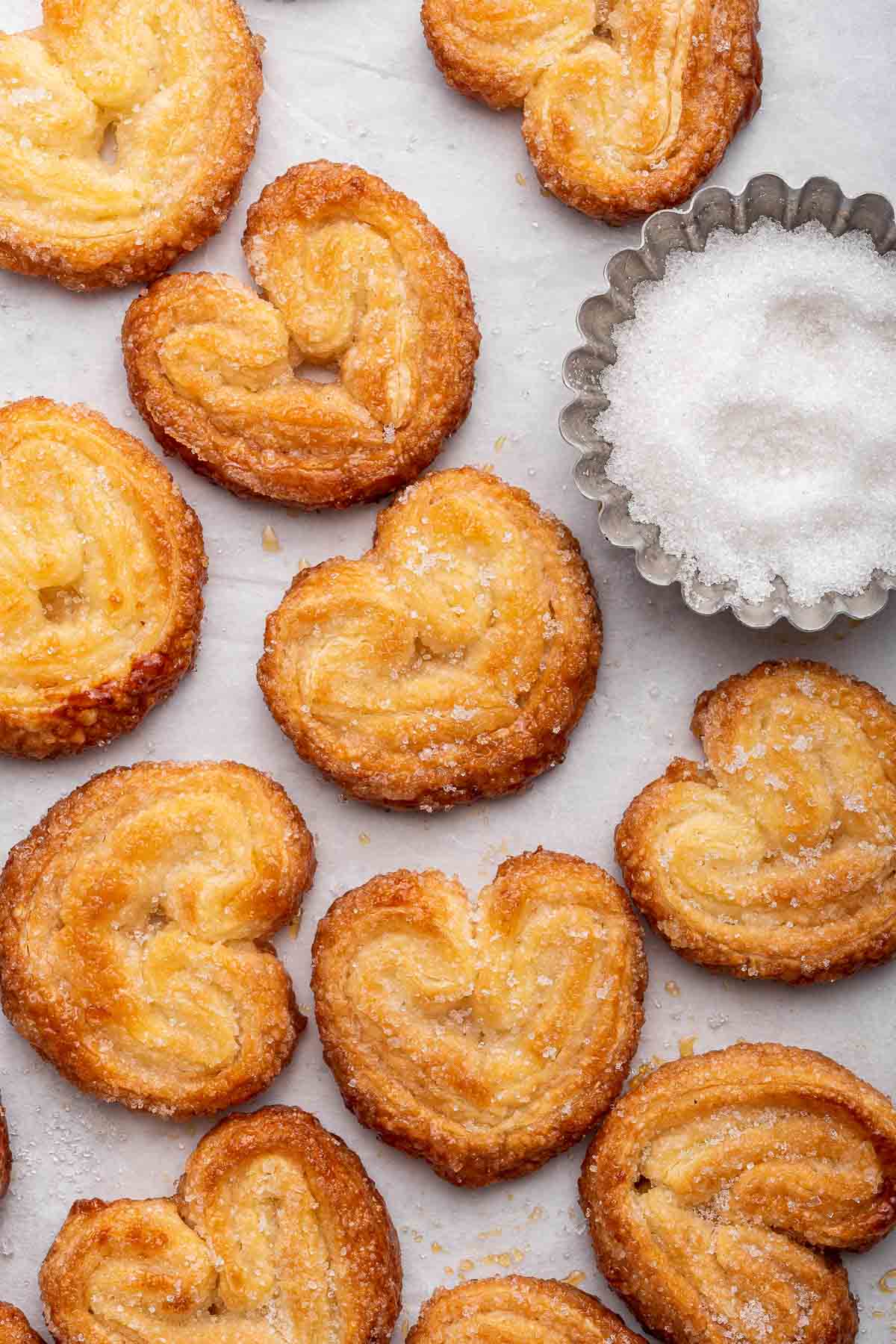 Overhead shot of heart shaped palmiers cookies with bowl of sugar on side.