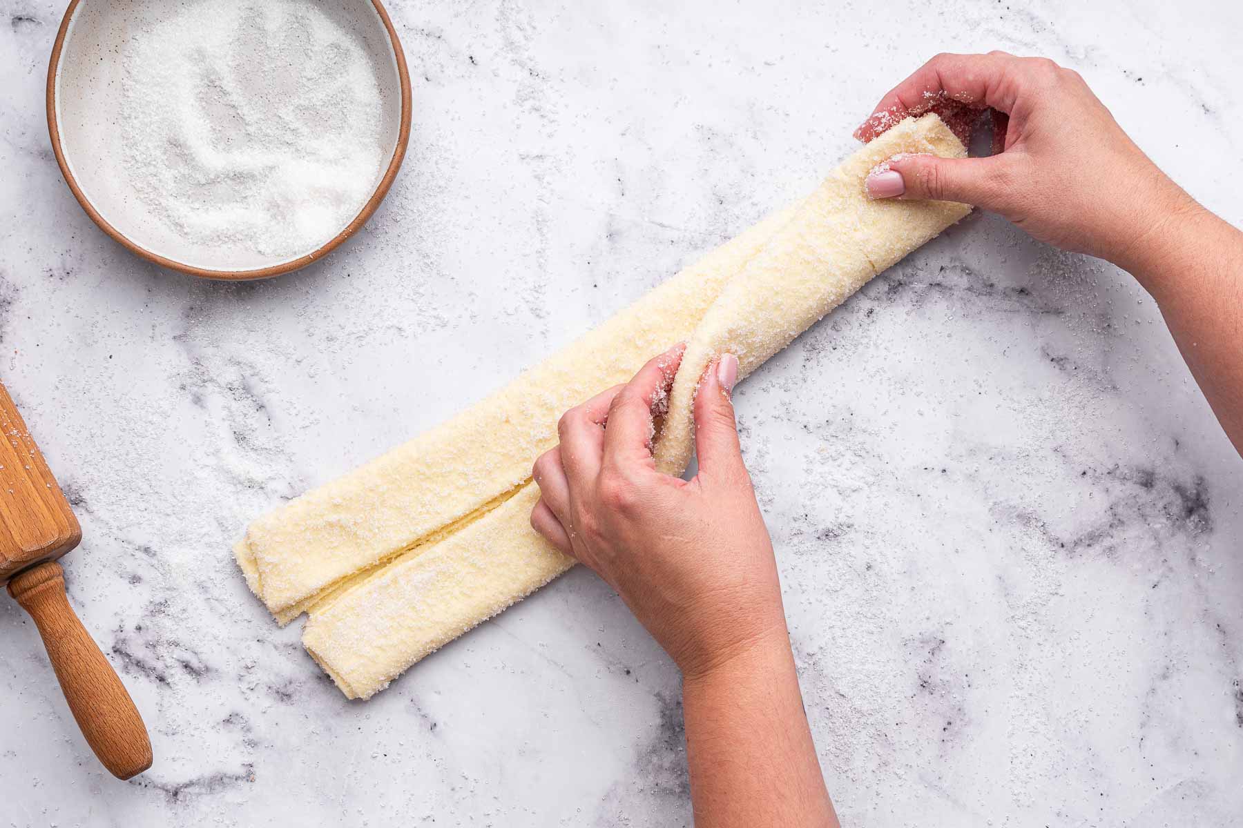 Hand folding puff pastry for palmier cookies on marble cutting board.