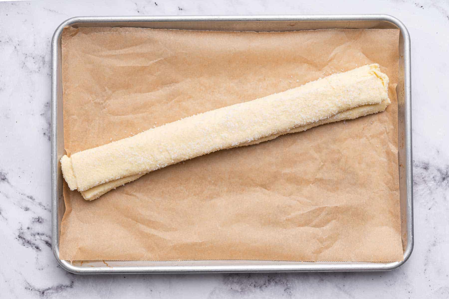Roll of dough on cookie sheet with brown parchment paper underneath.