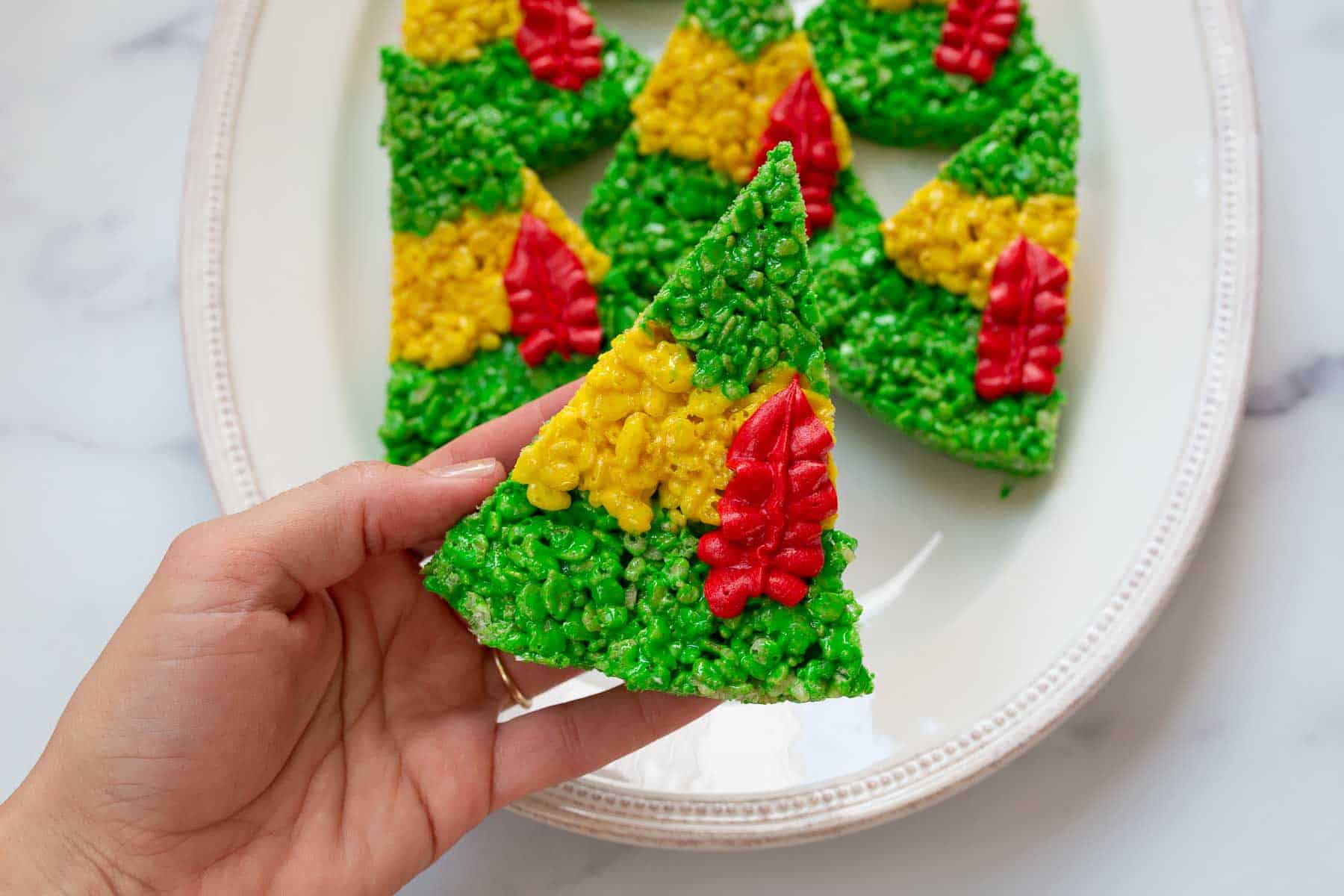 Hand holding buddy the elf hat Rice Krispie treats over a plate.