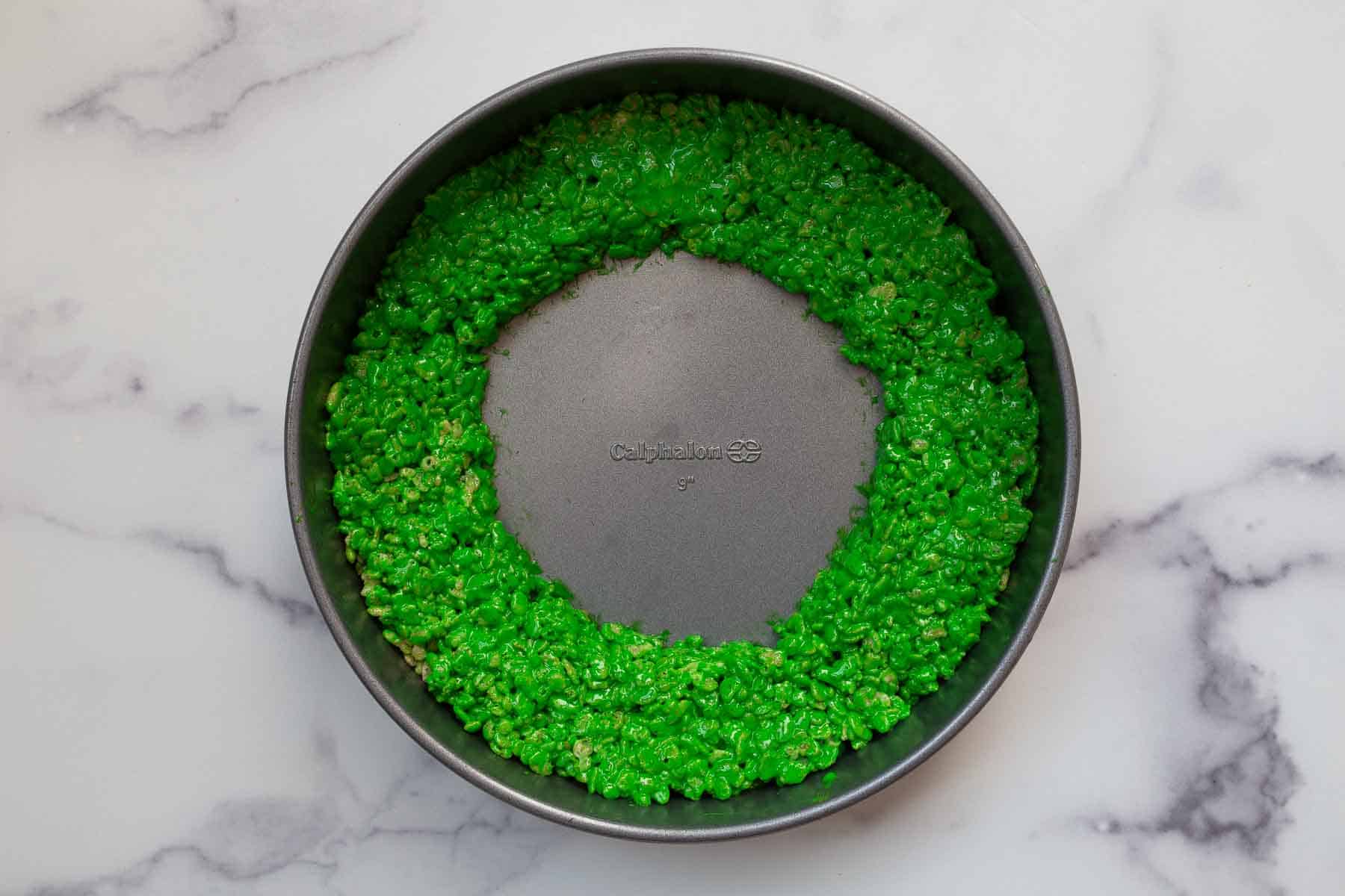 Ring of green rice cereal treats in a round cake pan.