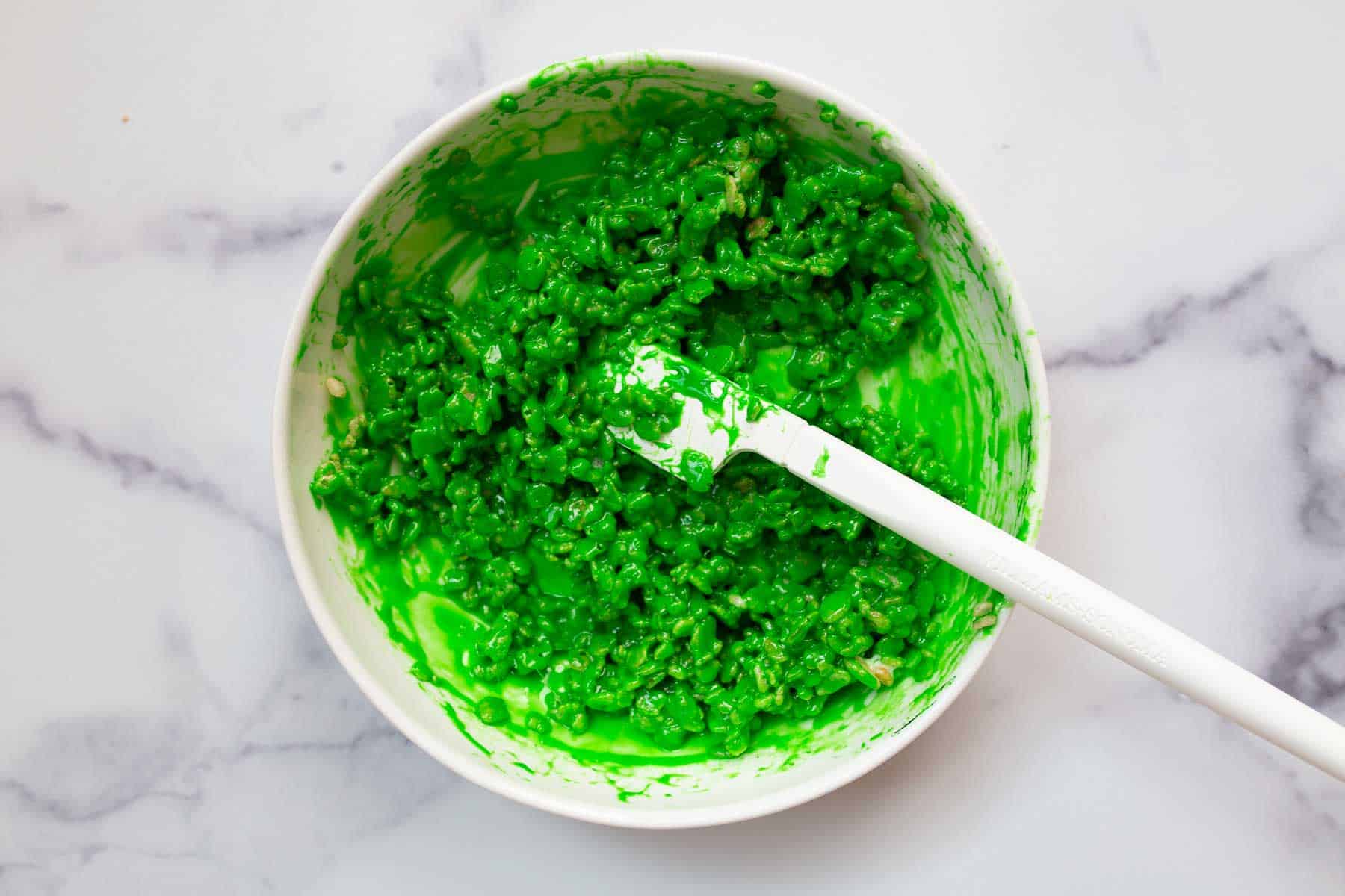 Rice Krispies dyed green in small white bowl with white spatula.