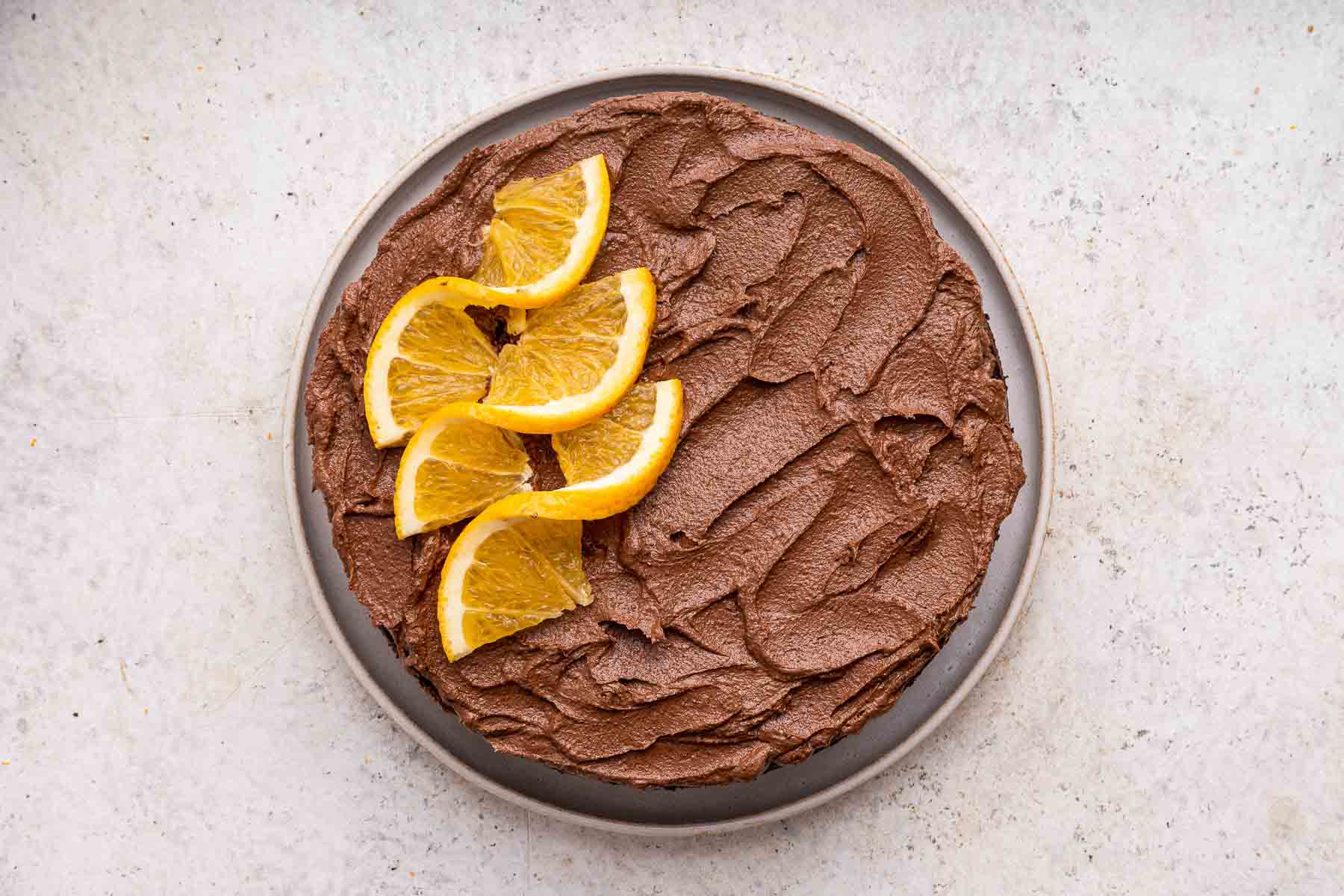 Decorating a chocolate orange cake with frosting and thinly sliced oranges.