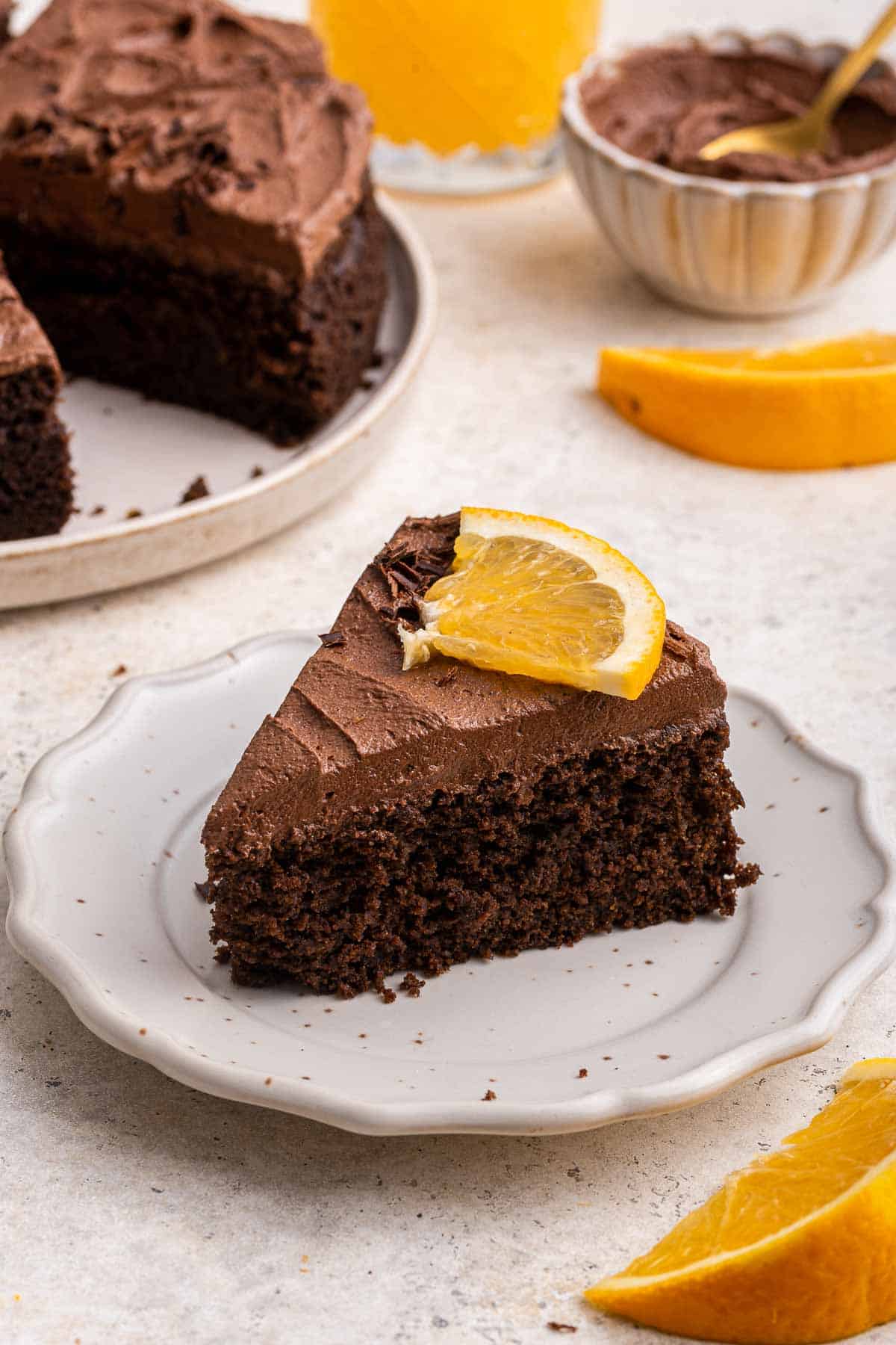 One slice of chocolate cake on a white plate with an orange slice on top.