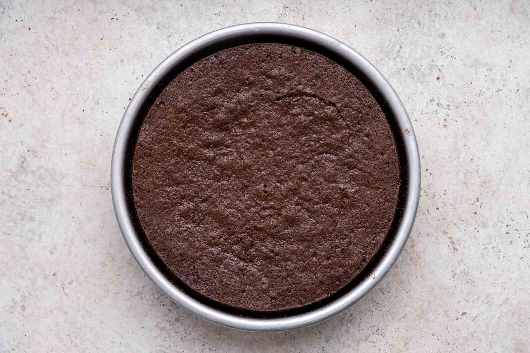 Freshly baked round brown cake in a metal pan.