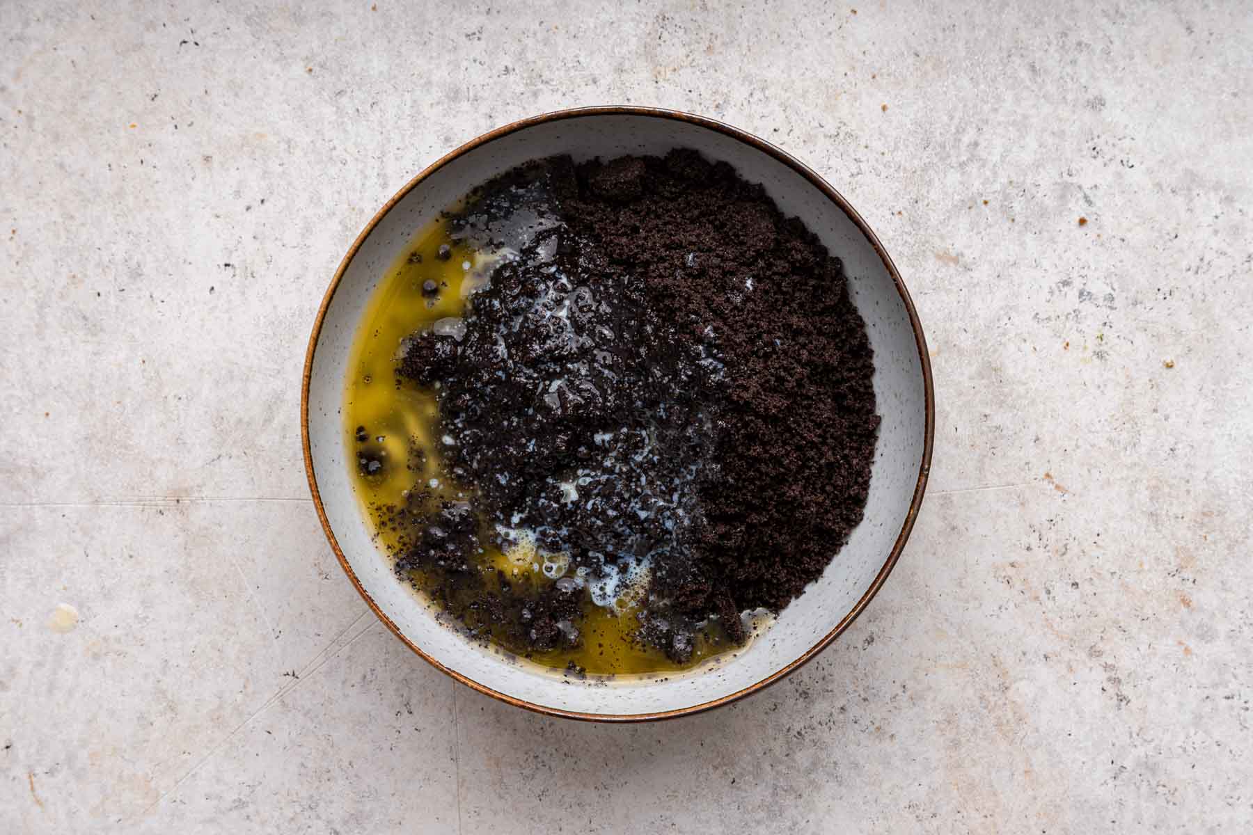 Crushed oreo crumbs in a bowl with yellow melted butter.