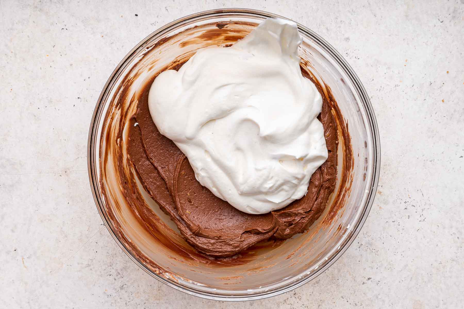 Folding white whipped cream into brown chocolate mixture in glass bowl.