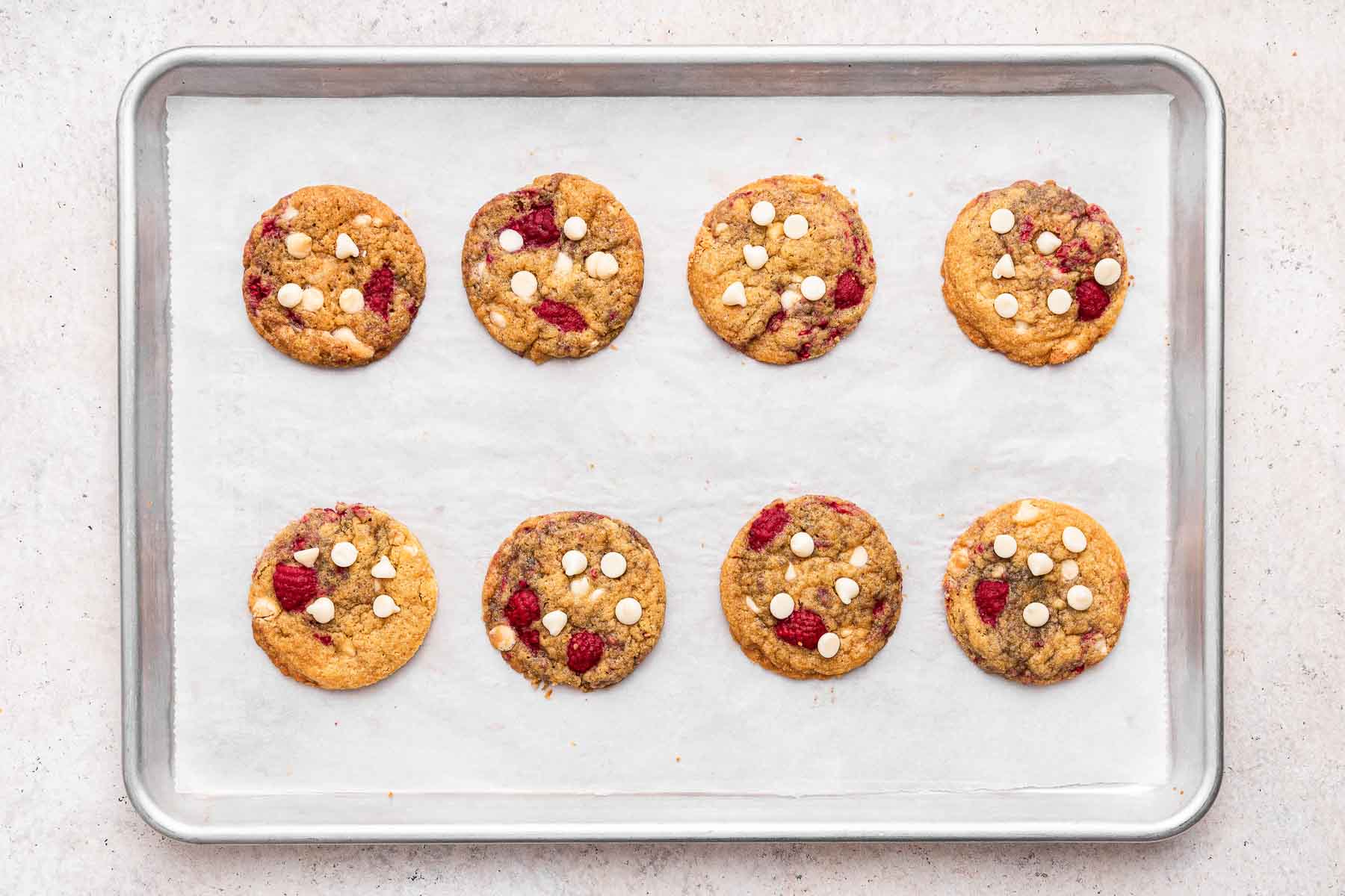 Freshly baked white chocolate chip raspberry cookies on a cookie sheet lined with parchment paper.