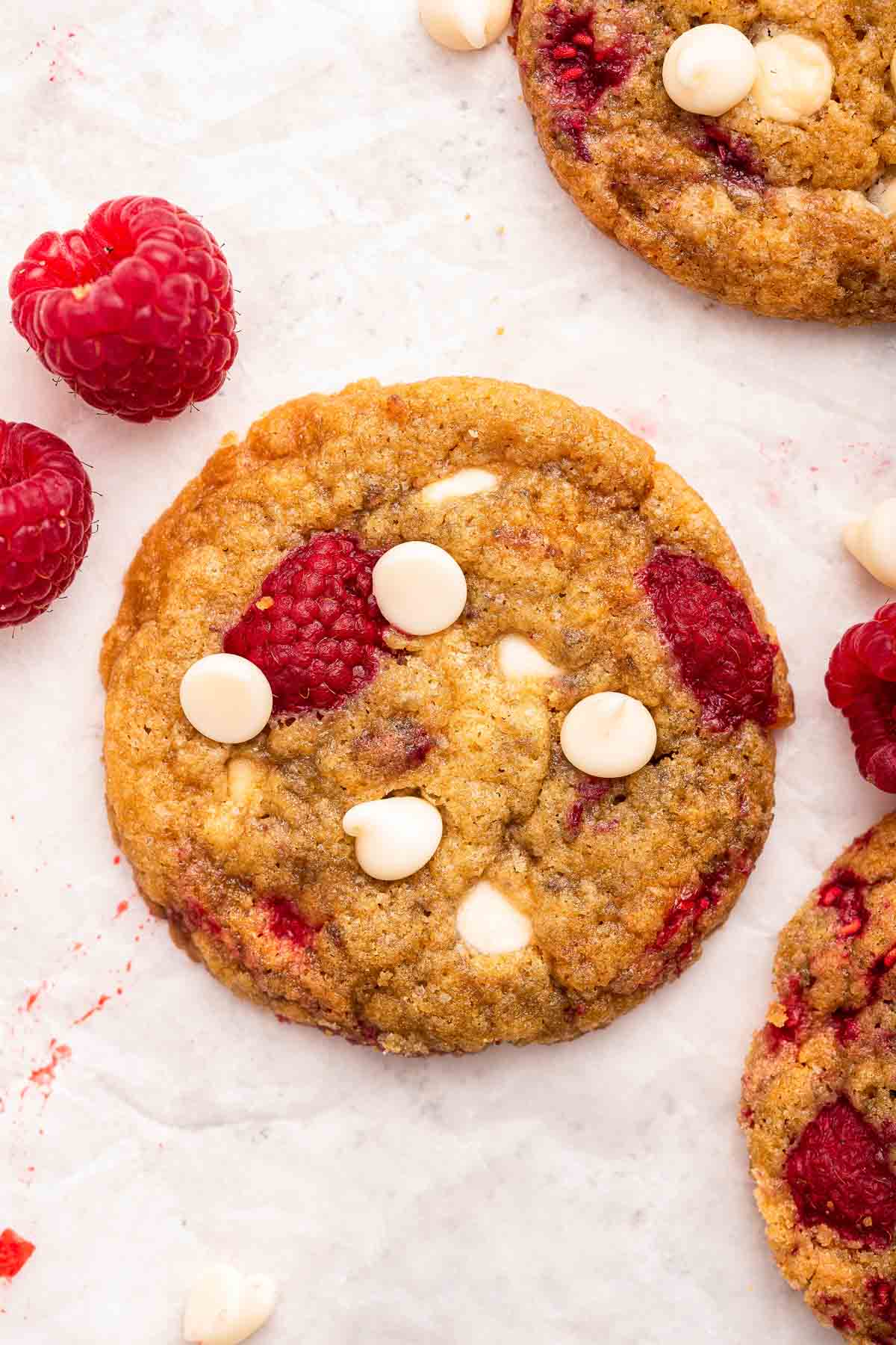 A single cookie on parchment paper with white chocolate chips and fresh raspberries on top.