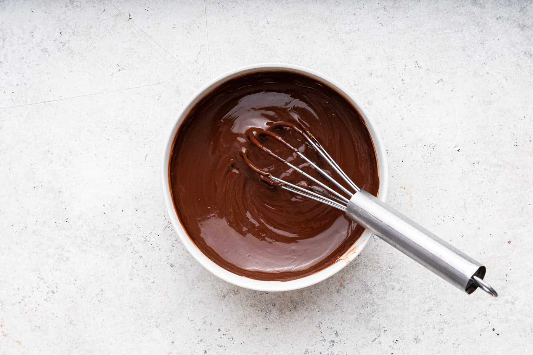 Melted chocolate in white bowl with a whisk.
