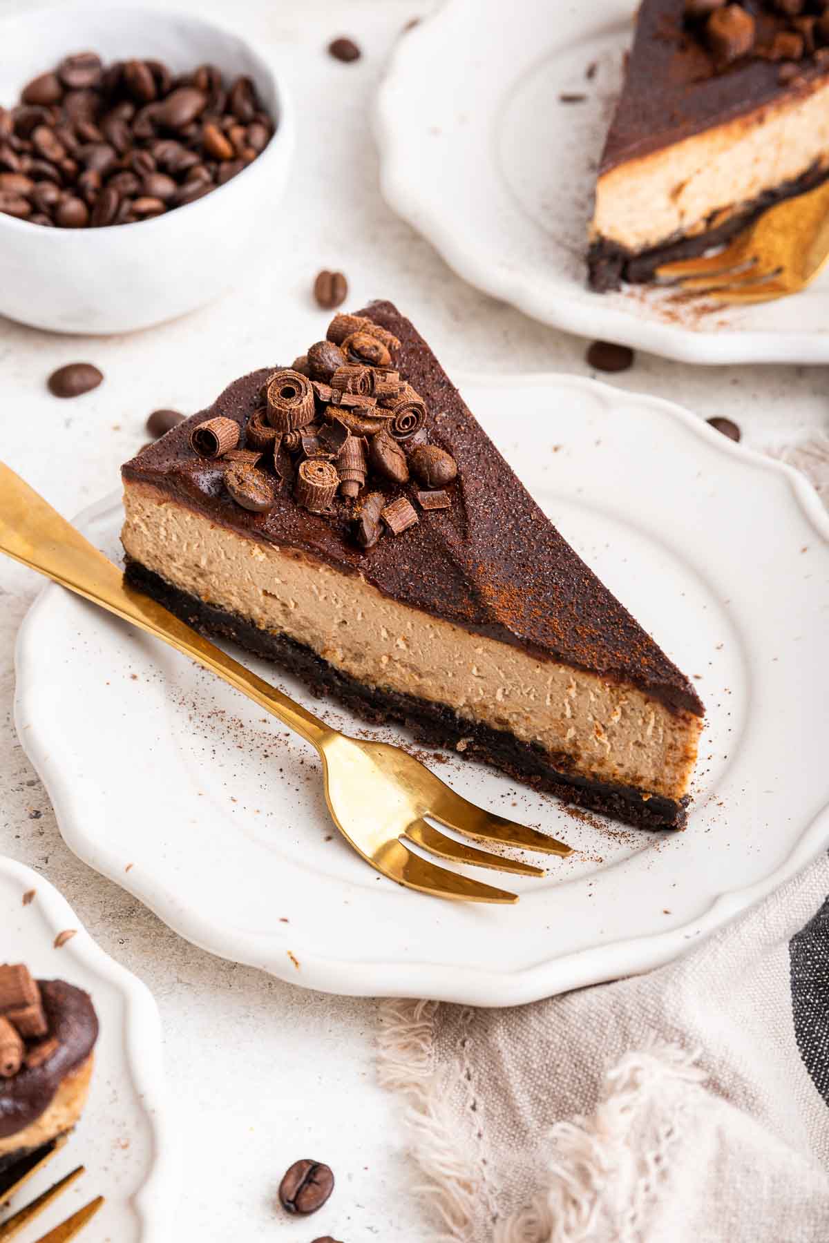 Slice of coffee cheesecake with chocolate ganache and gold fork on the side.