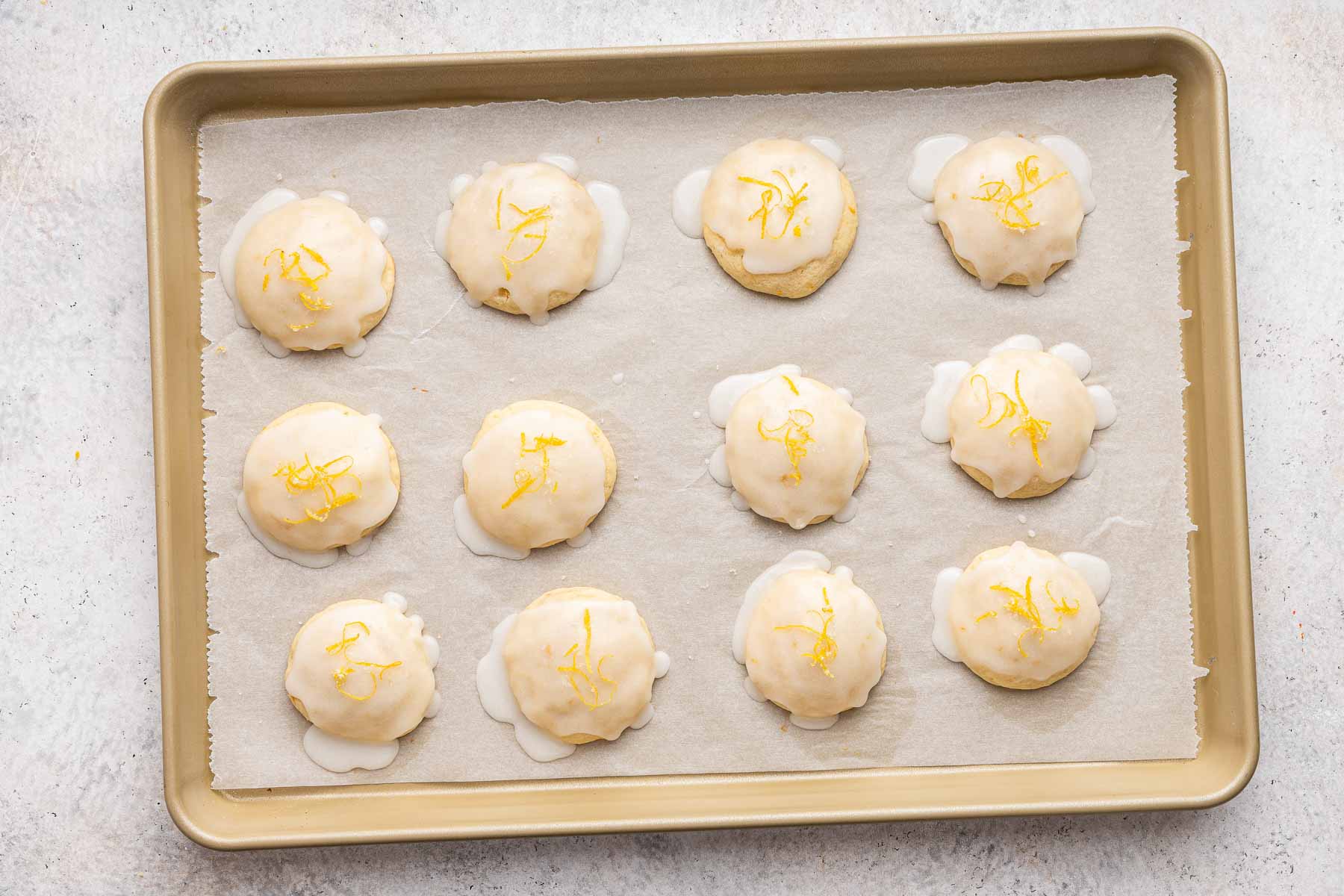 Frosted lemon ricotta cookies on a gold cookie sheet.